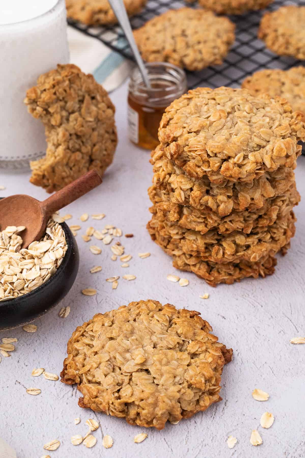 3 ingredient oatmeal cookies stacked with a small jar of honey, oats and cup of milk