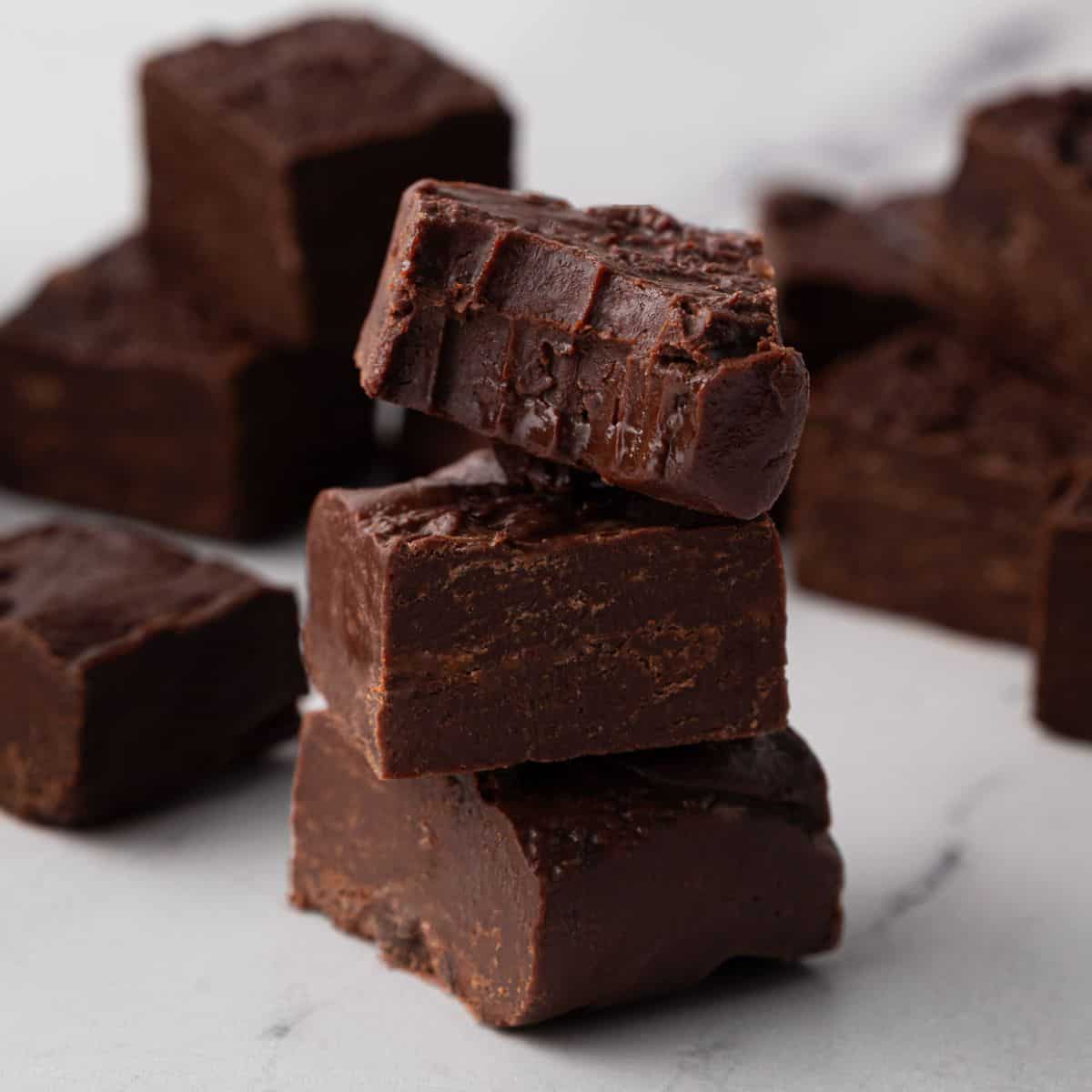 3 ingredient fudge stacked in a tower of 3 with the top piece of fudge with a bite taken out of it to show the texture.
