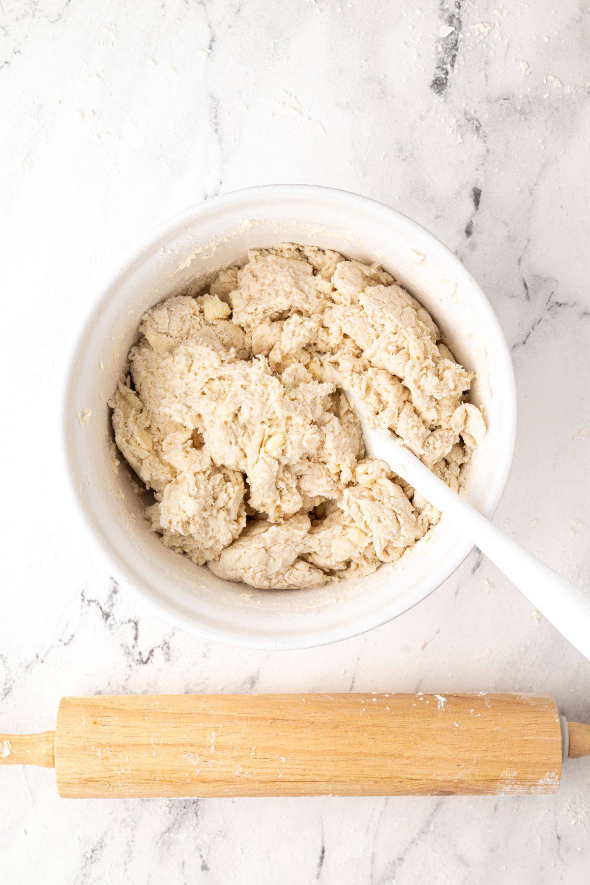A bowl of freshly mixed biscuit dough with a rolling pin placed below.