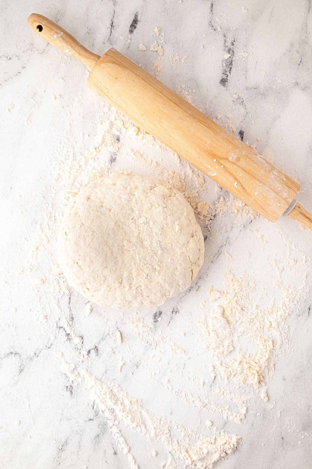 A ball of biscuit dough on a floured surface, with a wooden rolling pin beside it.