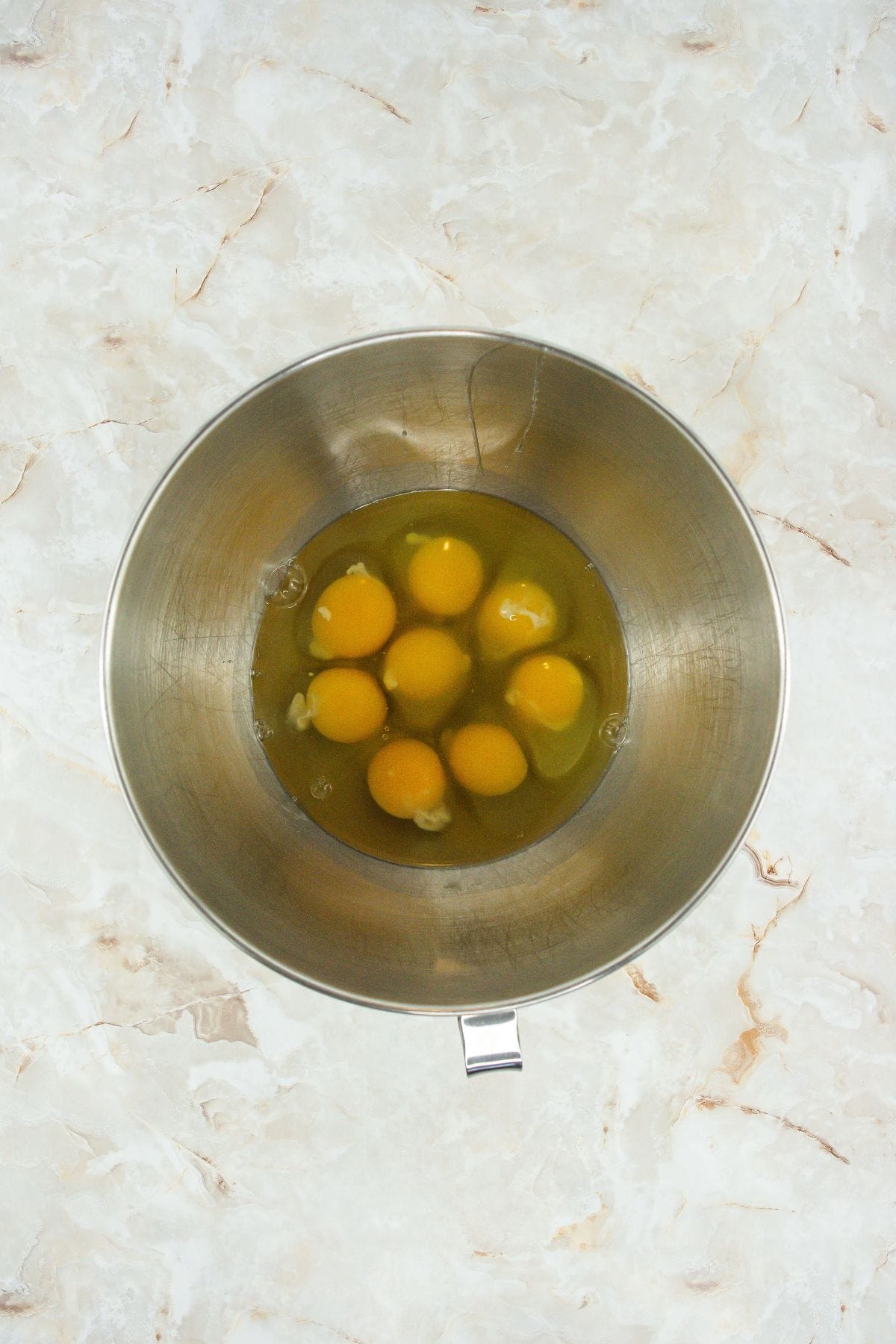 eight whole eggs with both yolks and whites visible in a stand mixer bowl