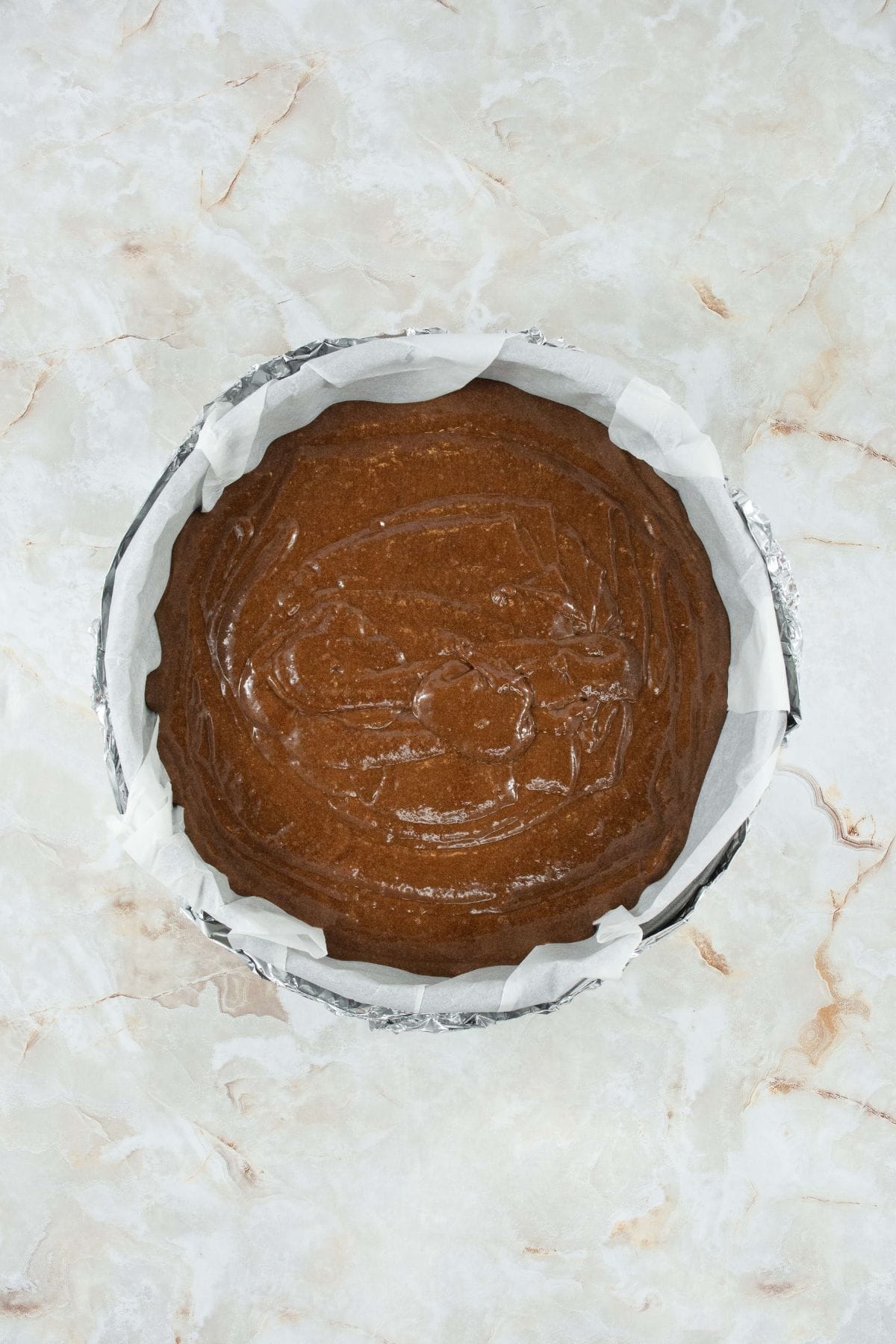 chocolate batter poured into a springform pan with parchment on the inside and several layers of foil on the outside