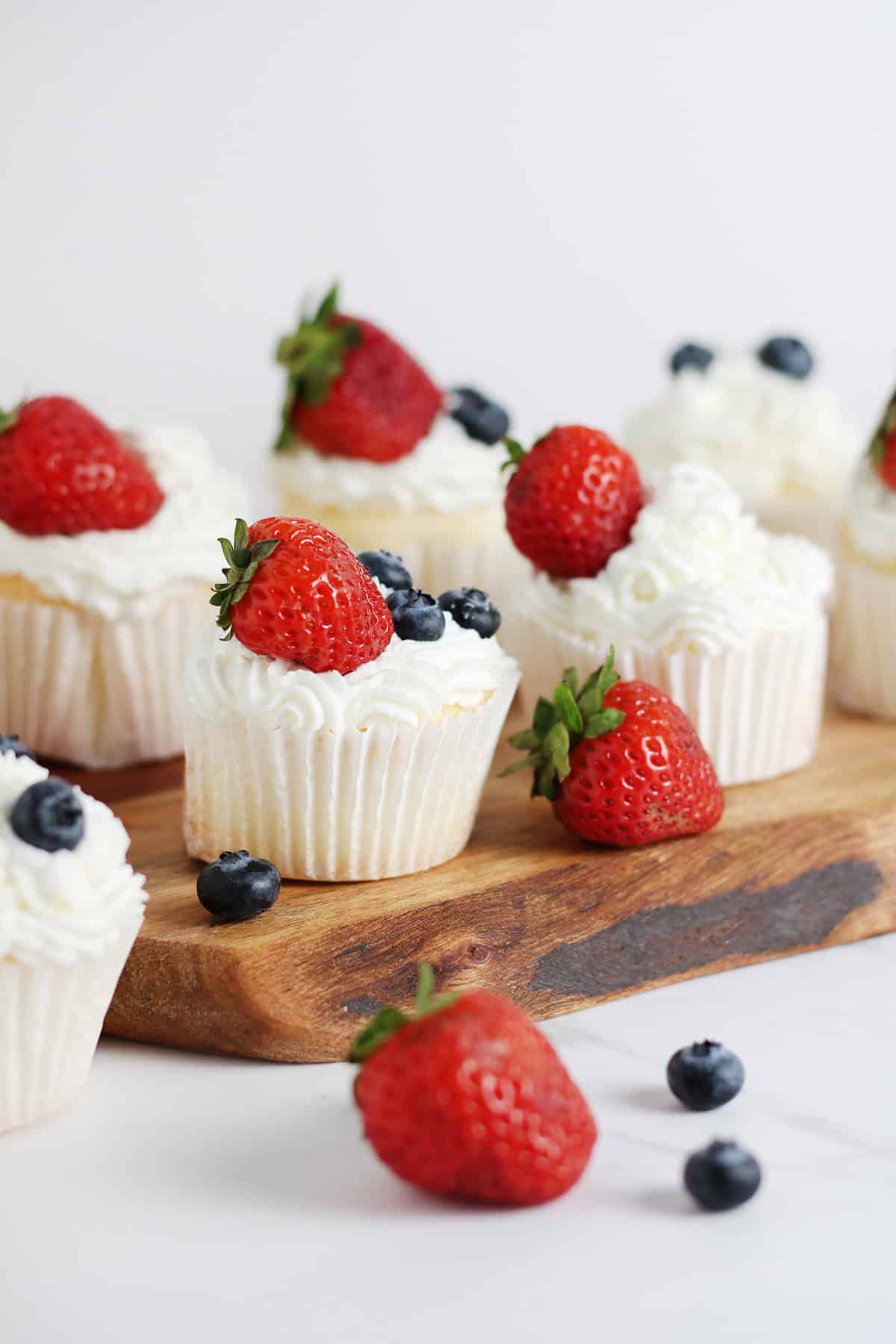 Angel food cake cupcakes topped with whipped cream and fresh berries on a wooden board