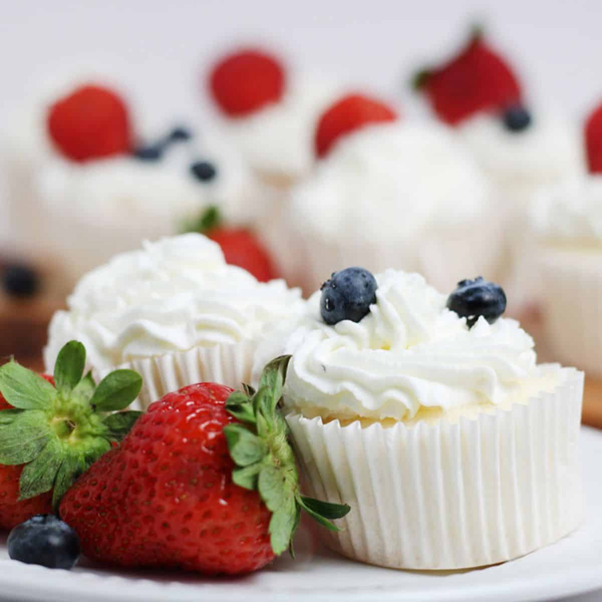 two angel food cake cupcakes topped with whipped cream and fresh blueberries on a white plate