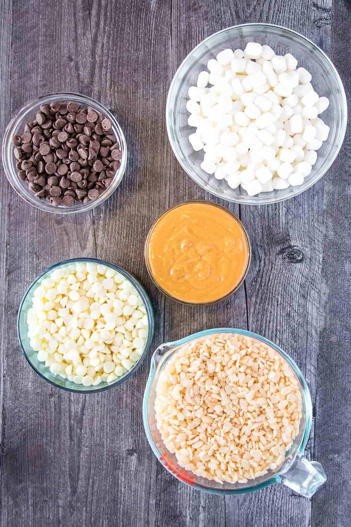 ingredients to make avalanche cookies: white chocolate chips, creamy peanut butter, rice krispies cereal, marshmallows, and chocolate chips