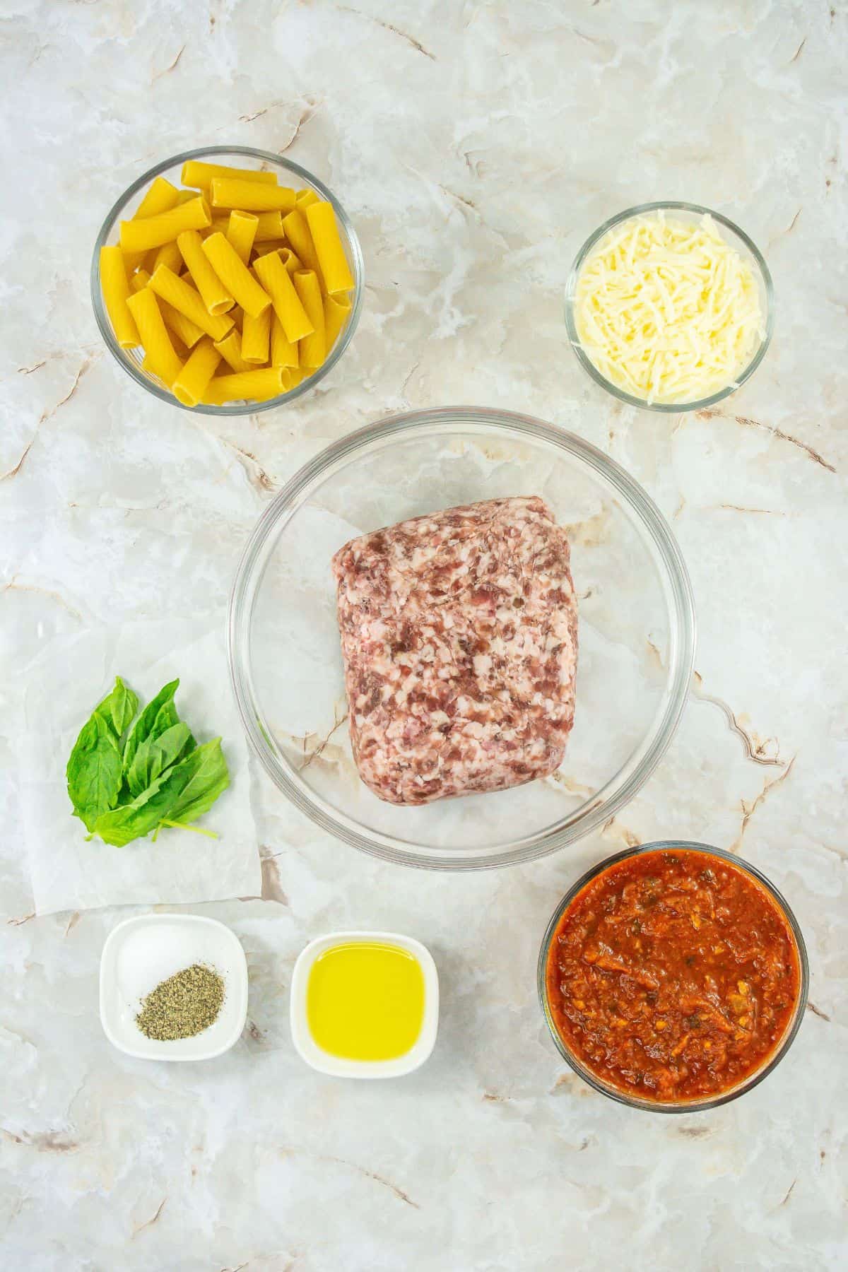 Ingredients laid out: Key ingredients for baked rigatoni, including pasta, ground meat, marinara sauce, cheese, olive oil, and seasoning, neatly arranged.
