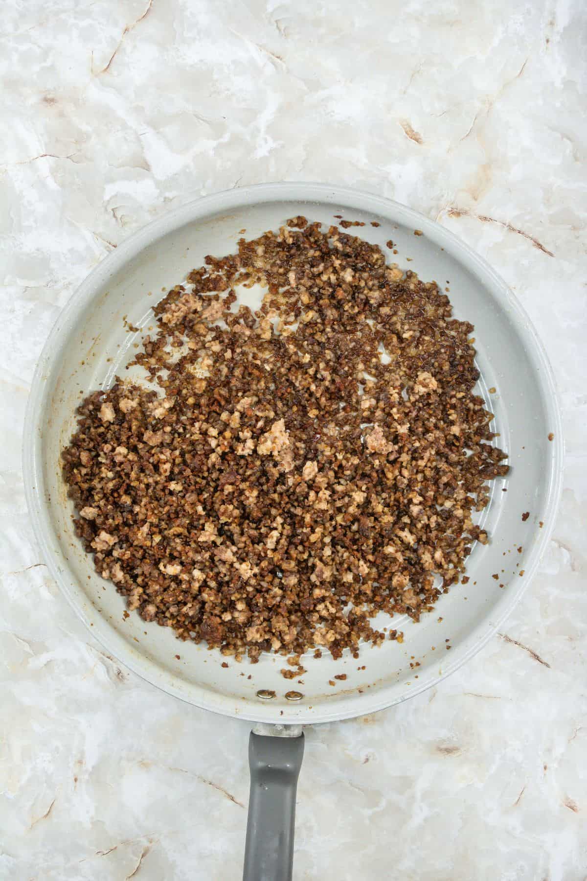 Ground meat browning in a skillet with visible seasoning and cooking oils.