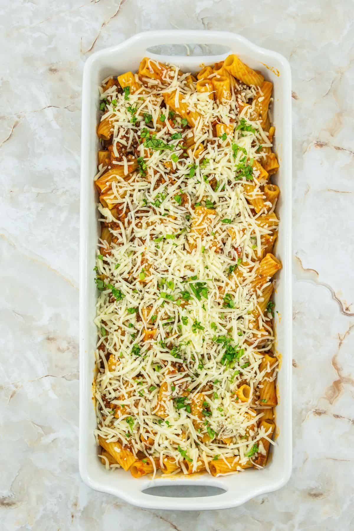 Rigatoni coated in sauce, topped with shredded cheese and fresh parsley, ready for the oven.