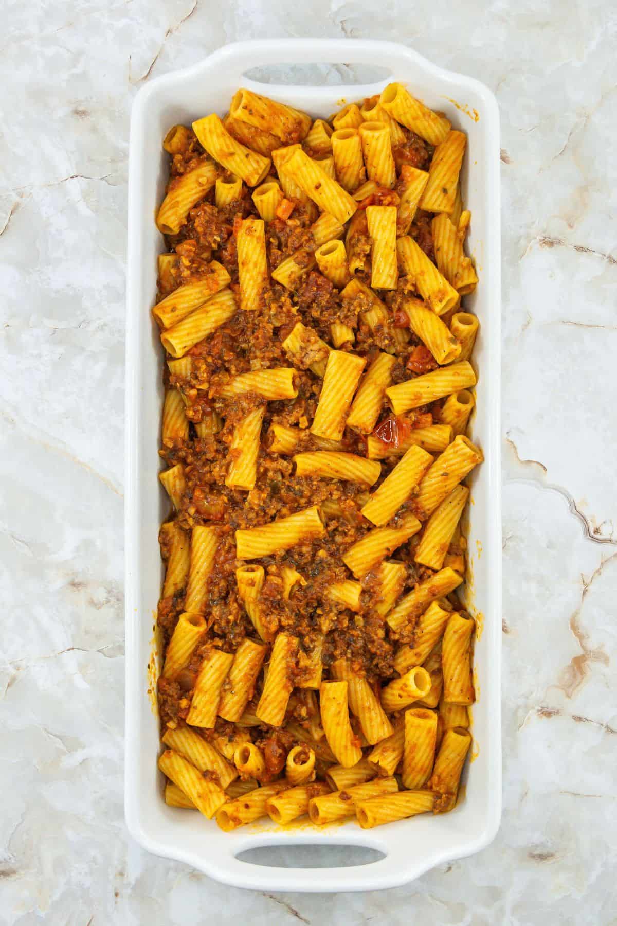 Unbaked rigatoni in the dish: Rigatoni mixed with sauce and meat, ready to be baked.