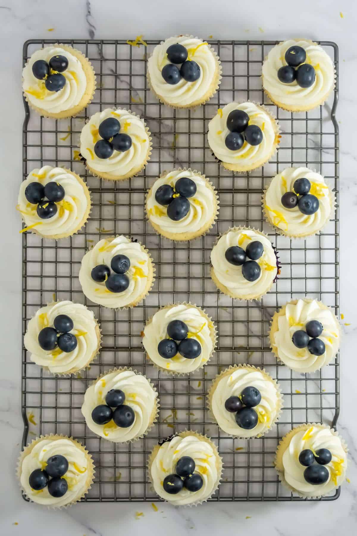 Decorated blueberry lemon cupcakes with frosting, fresh blueberries, and lemon zest on a cooling rack.