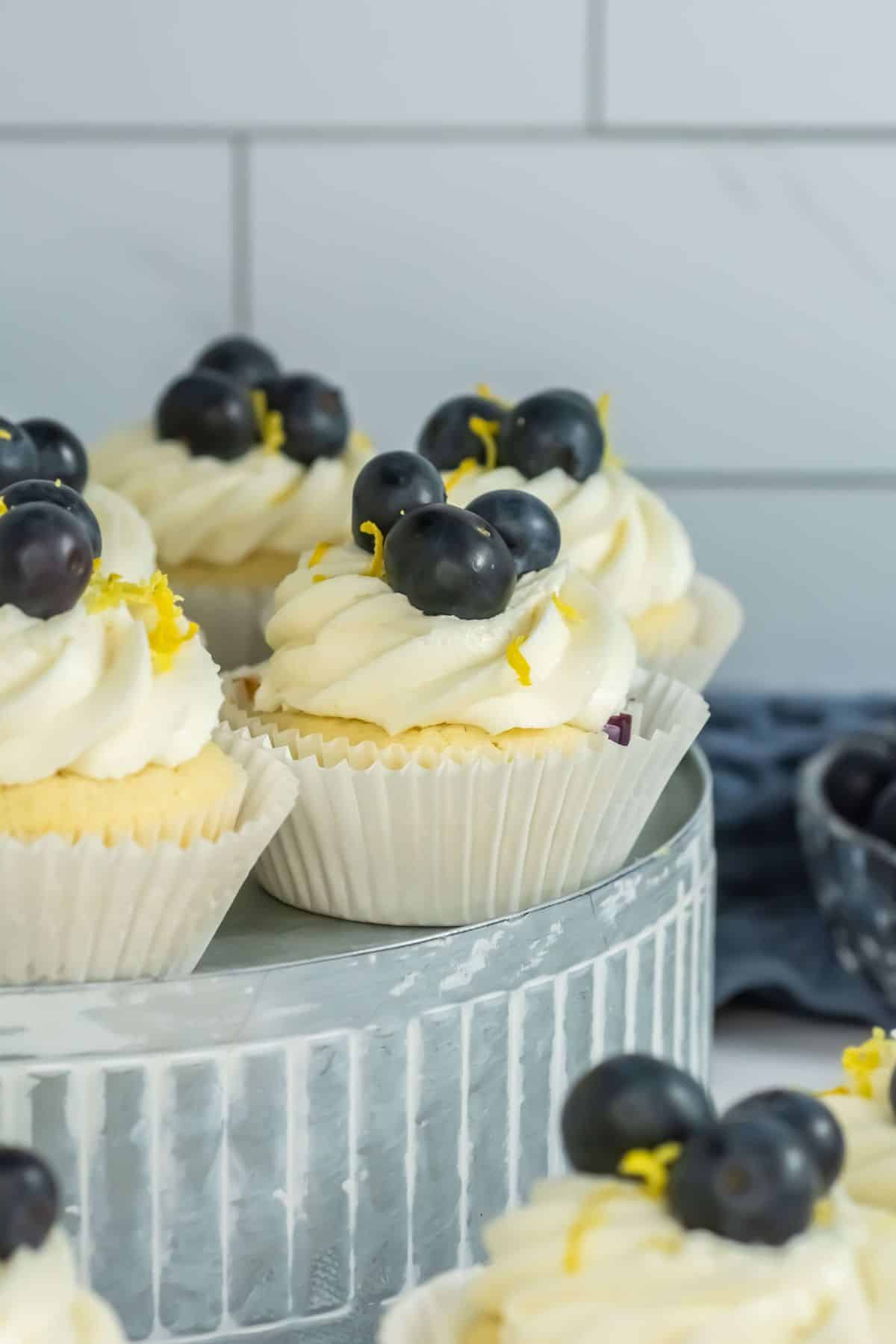 A close-up shot of fully decorated cupcakes, topped with whipped frosting, blueberries, and lemon zest