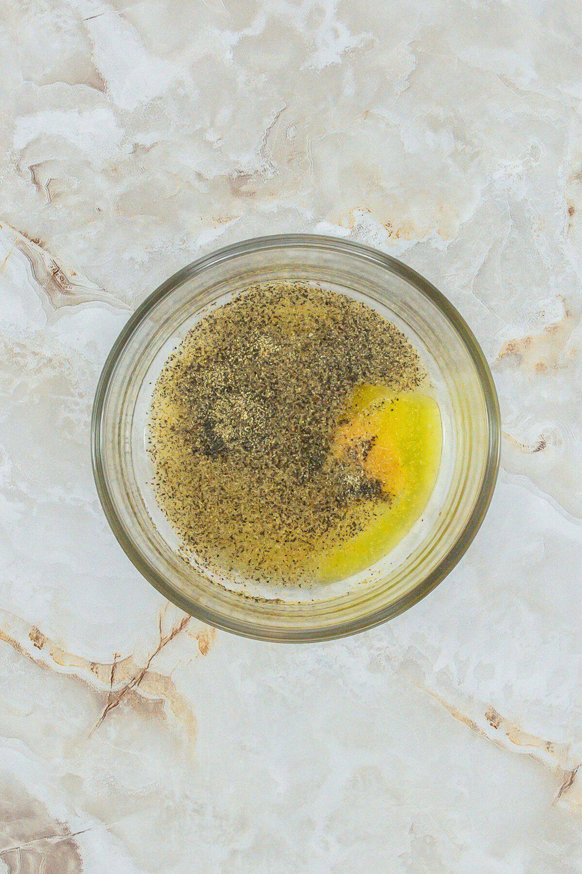 A small bowl with melted butter or oil mixed with seasonings, ready for marinade or basting.