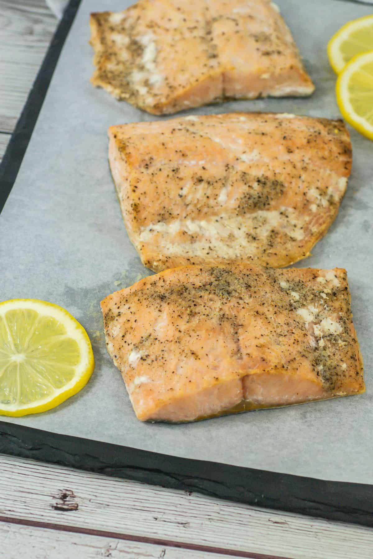 Close-up of broiled salmon on a serving tray with a lemon slice as garnish.