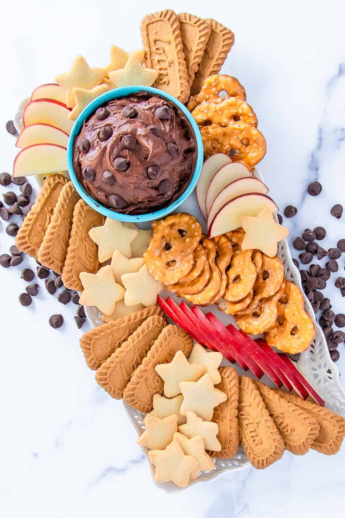 fruit, cookies, and pretzels surrounding a cup of brownie batter dip topped with chocolate chips