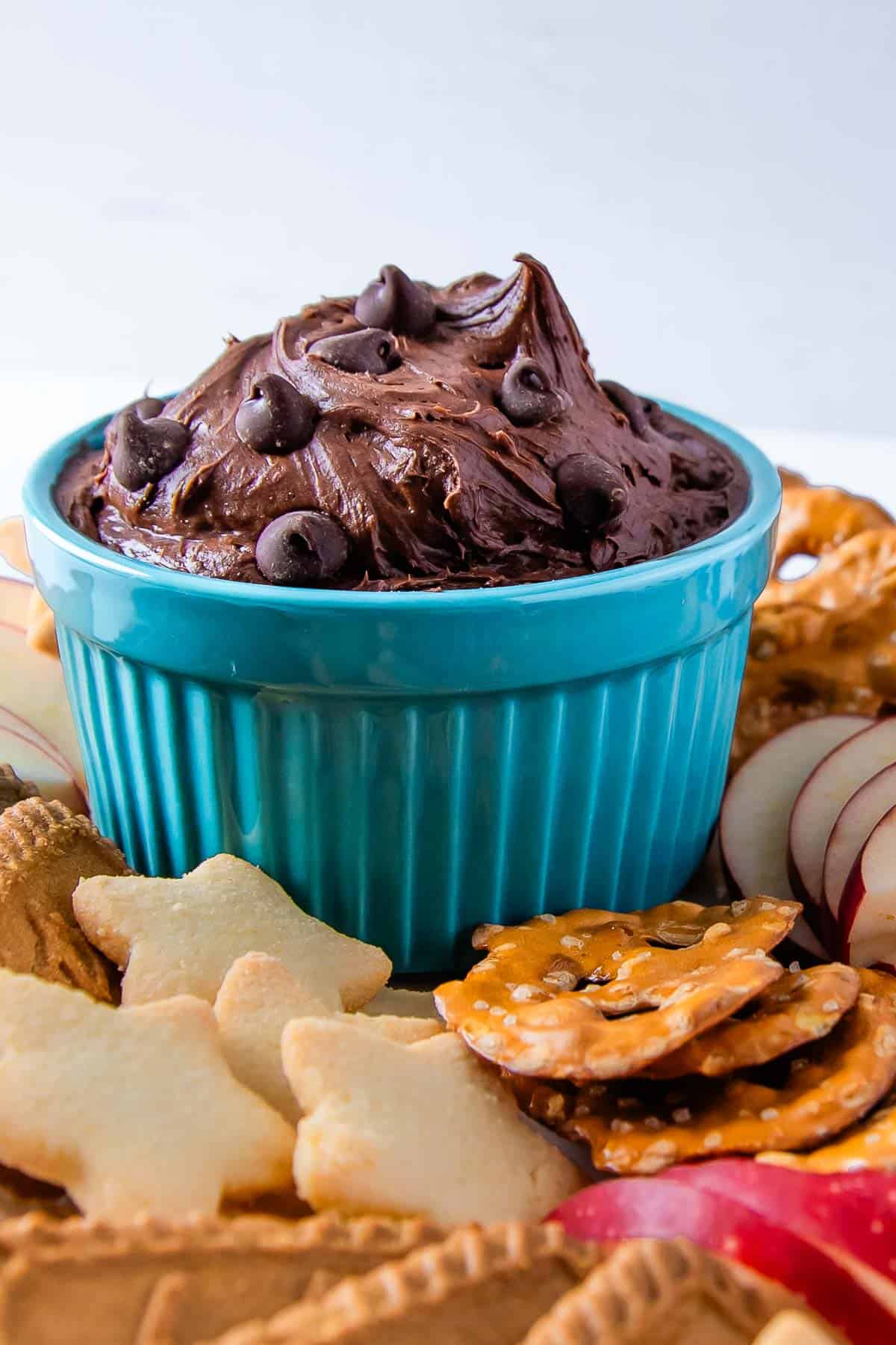 close-up shot of a cup of brownie batter dip surrounded by fruit, cookies, and pretzels