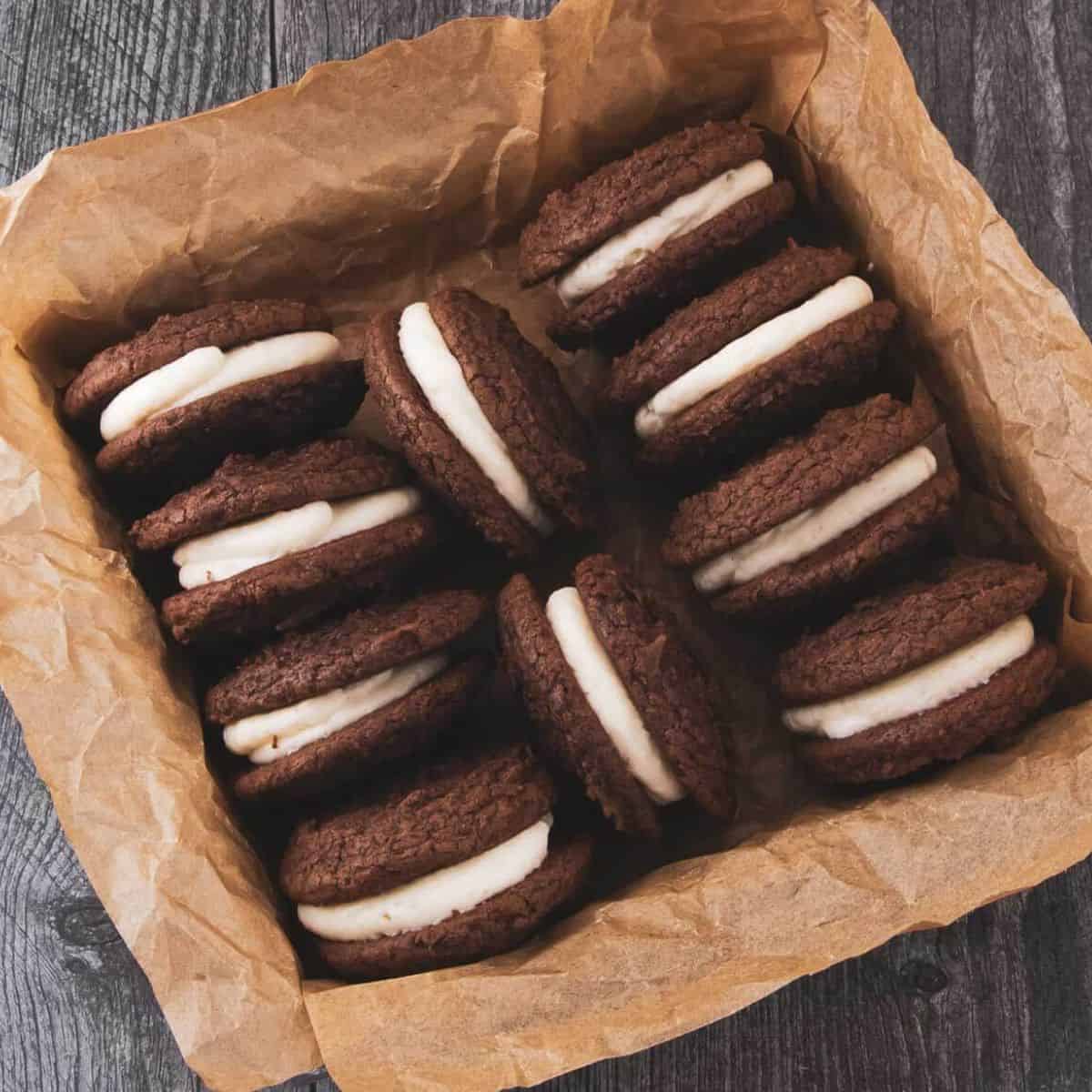 Chocolate brownie cookies sandwiched with a creamy filling, arranged in a parchment-lined box.