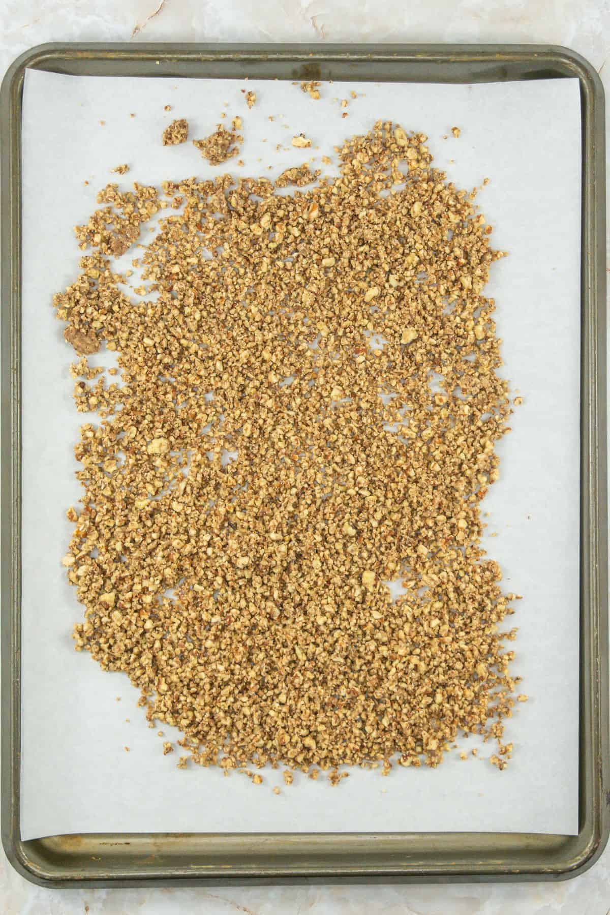 A baking tray lined with parchment paper, topped with evenly spread toasted, chopped pecans. The pecans are golden-brown, indicating they have been freshly toasted.