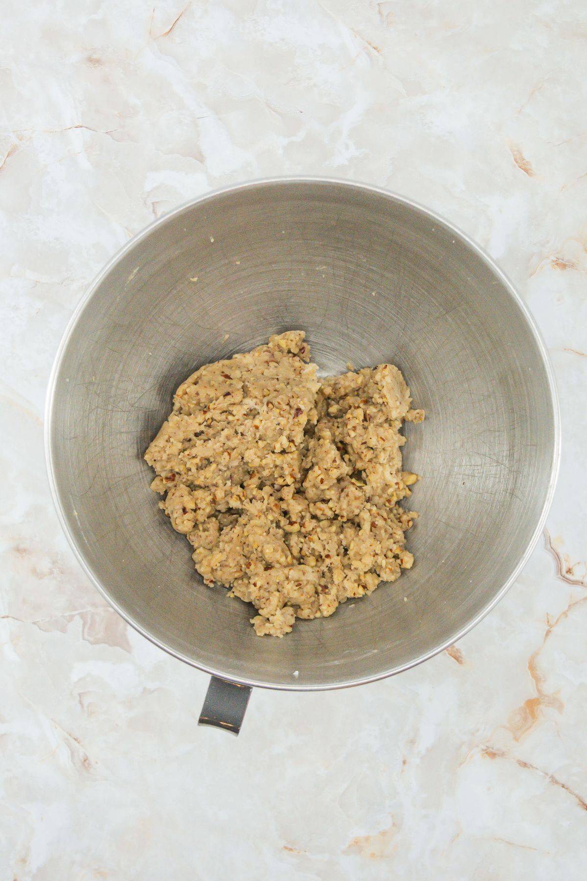 A mixing bowl containing fully combined dough for the Butter Pecan Meltaways. The dough has a coarse, textured appearance from the pecans.