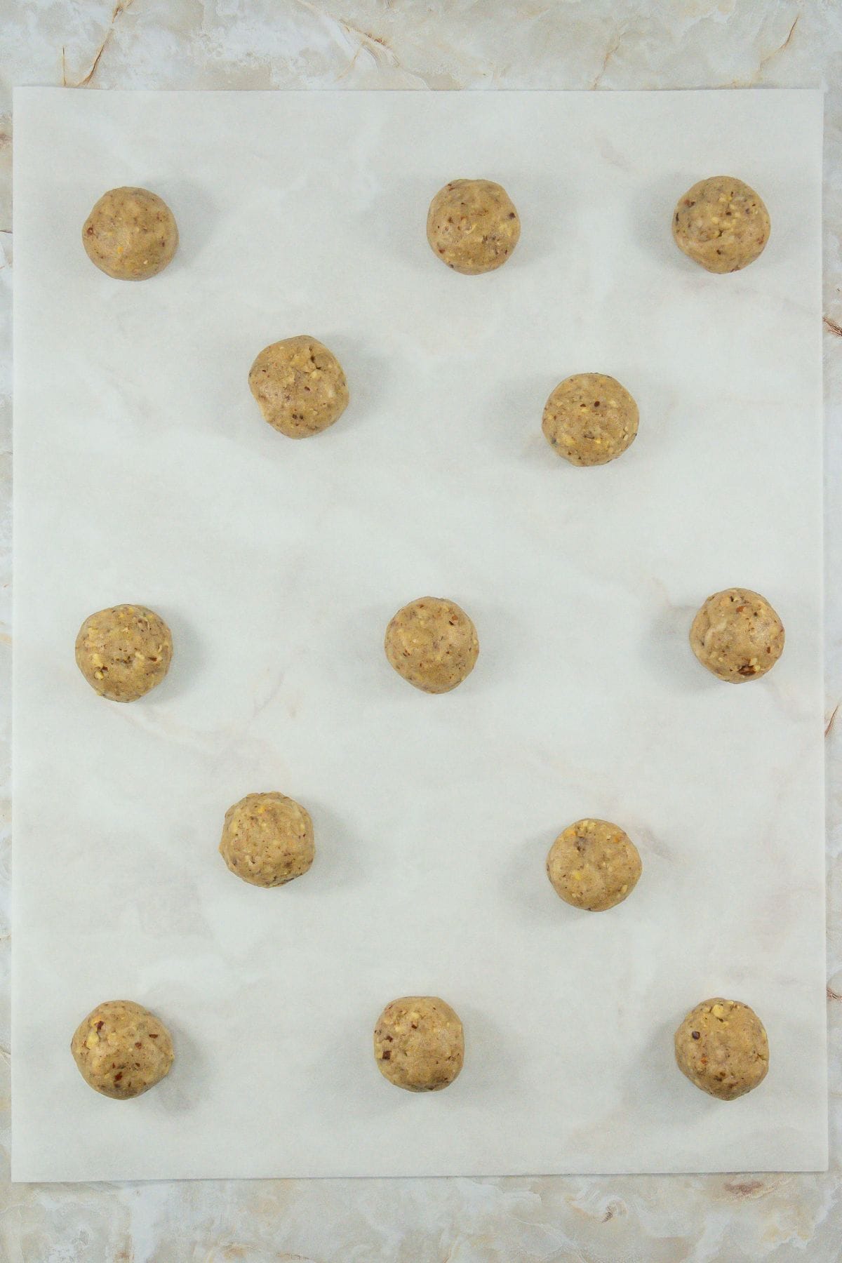 A parchment-lined baking sheet holding uniformly rolled cookie dough balls, evenly spaced and ready for baking.