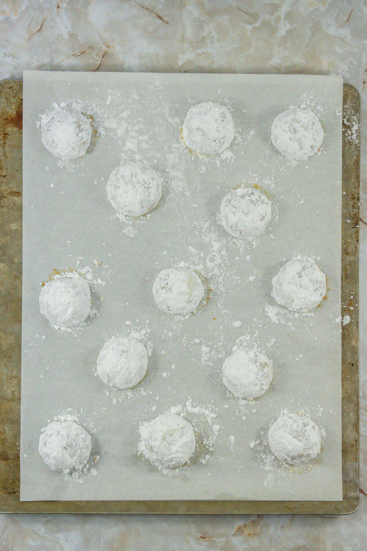 The baked Butter Pecan Meltaways, dusted generously with powdered sugar, resting on a parchment-lined baking sheet. The cookies look soft and delicately crumbly.