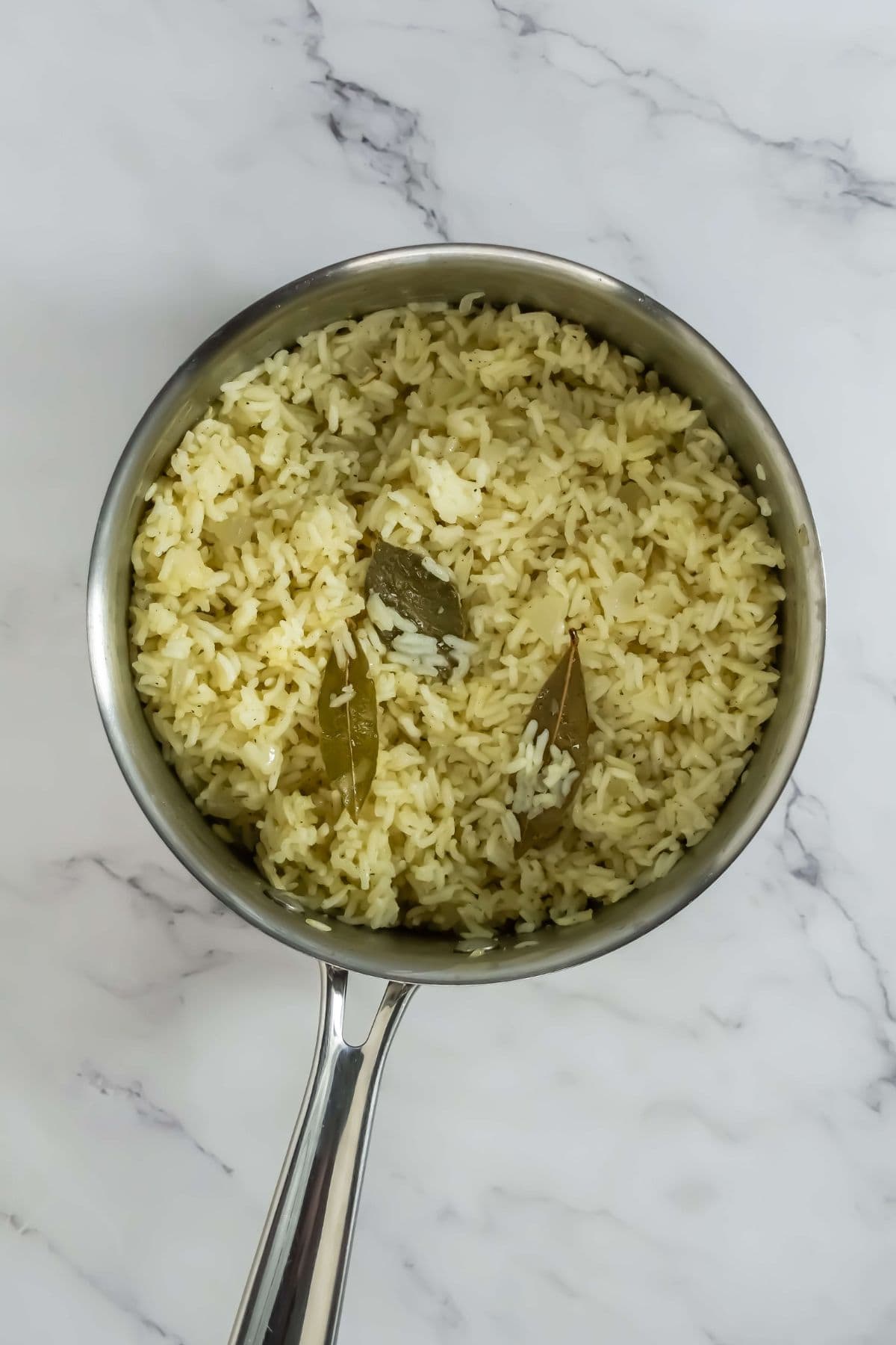 Cooked buttered rice in a saucepan with bay leaves.
