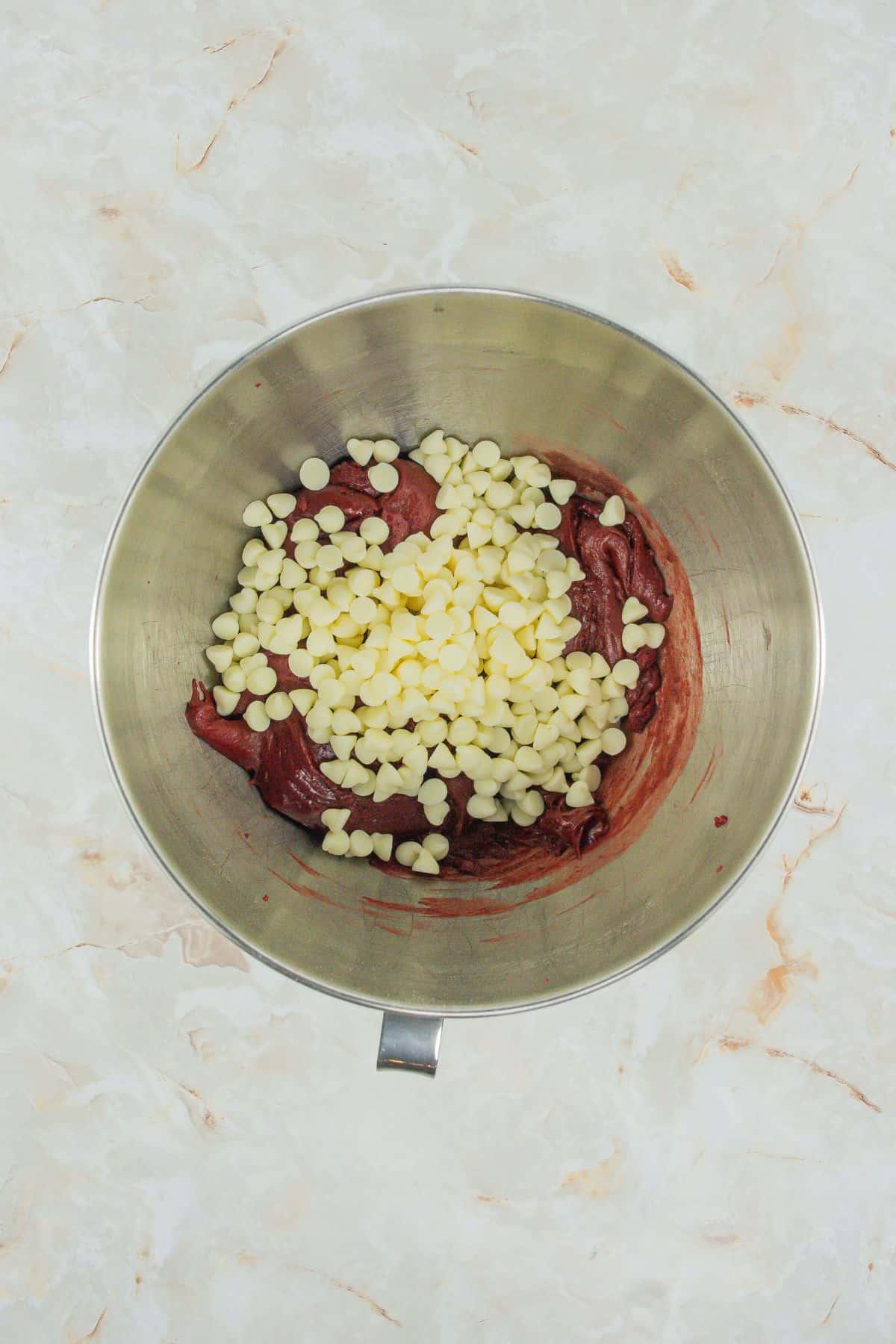 Another angle showing a generous amount of white chocolate chips being added to the batter, emphasizing the rich, chocolate-filled texture of the cookies.