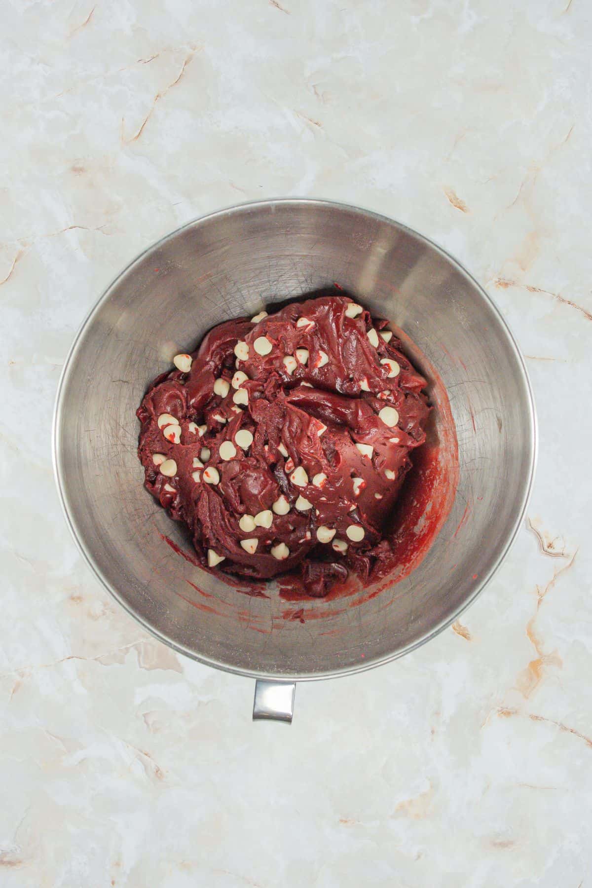 A mixing bowl containing the thick, red velvet cookie batter mixed with white chocolate chips.