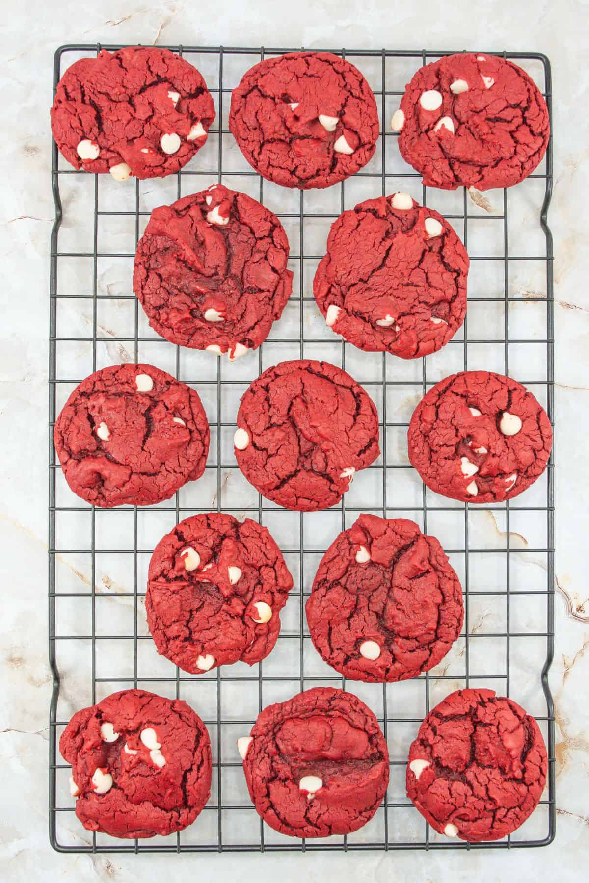 Fully baked red velvet cookies with white chocolate chips cooling on a wire rack. The vibrant red color and melty white chips give them a festive appearance.