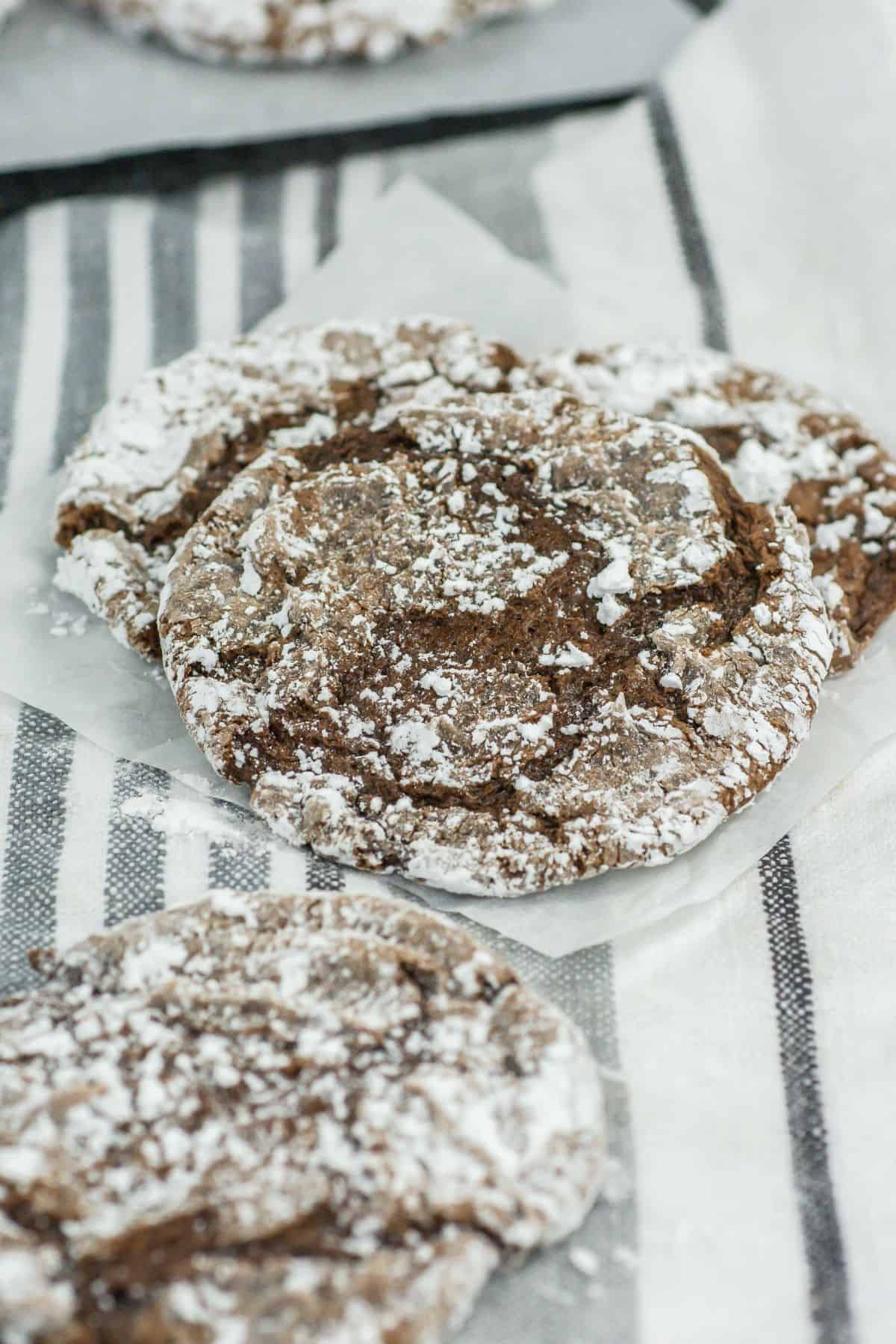 A slate tray holding several chocolate crinkle cookies. The cookies are neatly arranged, and the powdered sugar contrasts beautifully with the dark chocolate color.