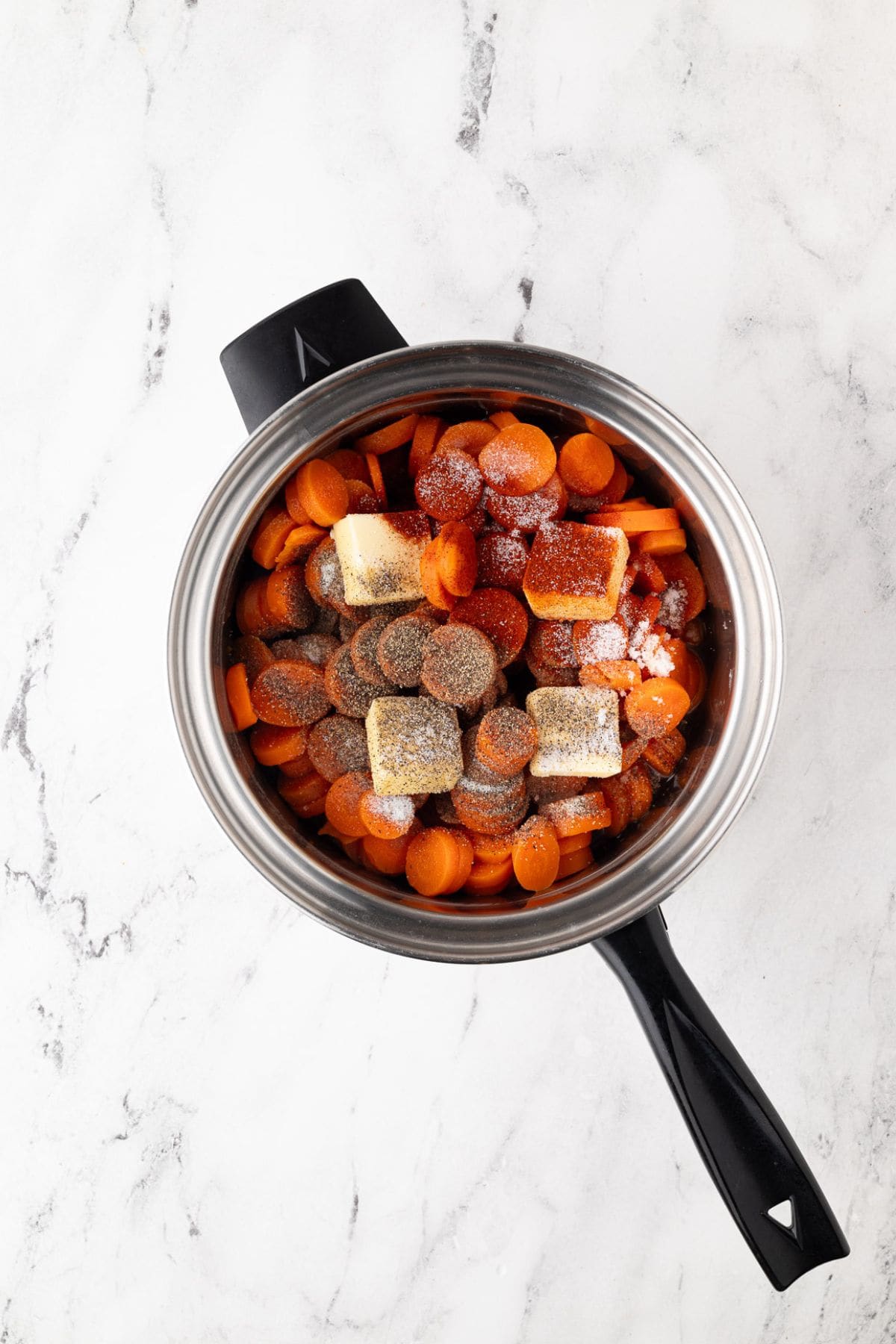 Raw carrot slices in a saucepan with butter and seasonings before cooking.