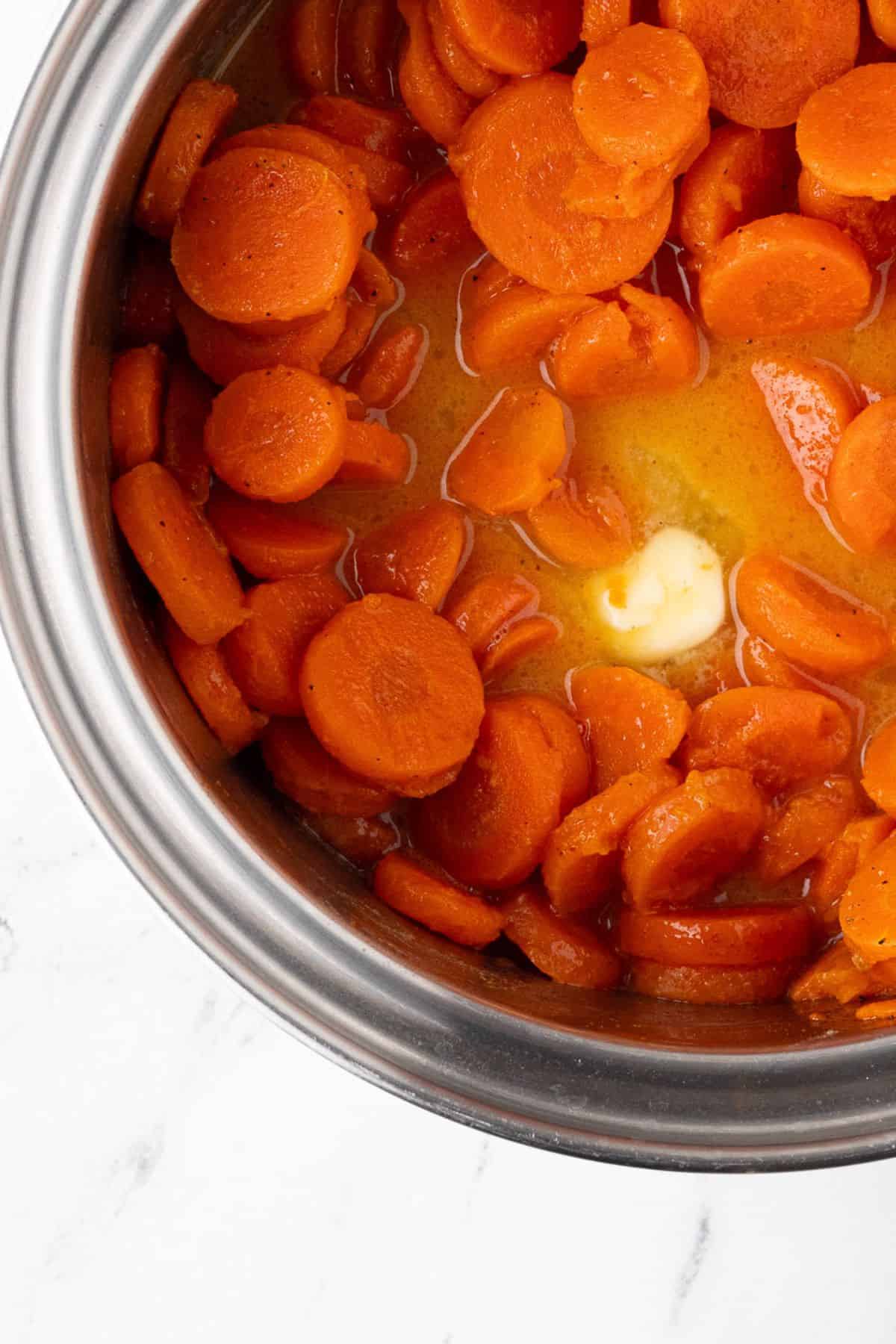 A close-up view of cooked carrot slices in a stainless steel pot, glistening with butter and seasoning.