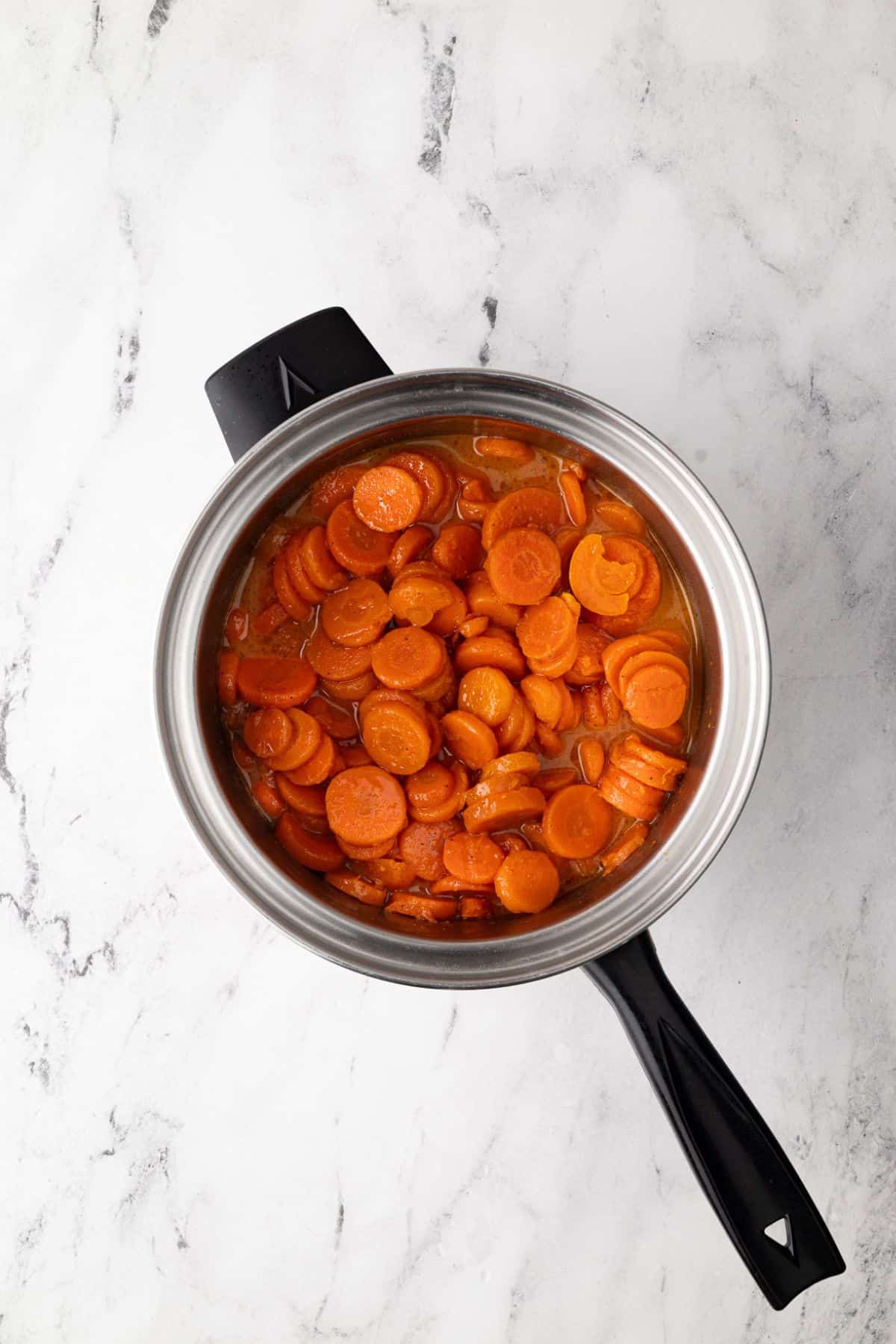 Cooked carrots in a saucepan, showing their glossy, tender texture with a light sauce.
