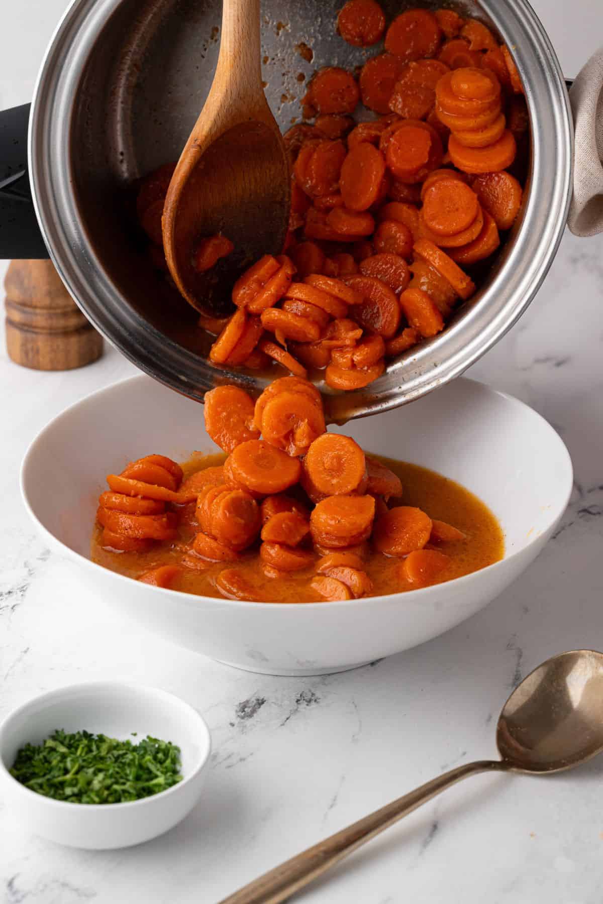Cooked carrots being transferred from a pot to a serving bowl, showing the vibrant orange and juicy sauce.