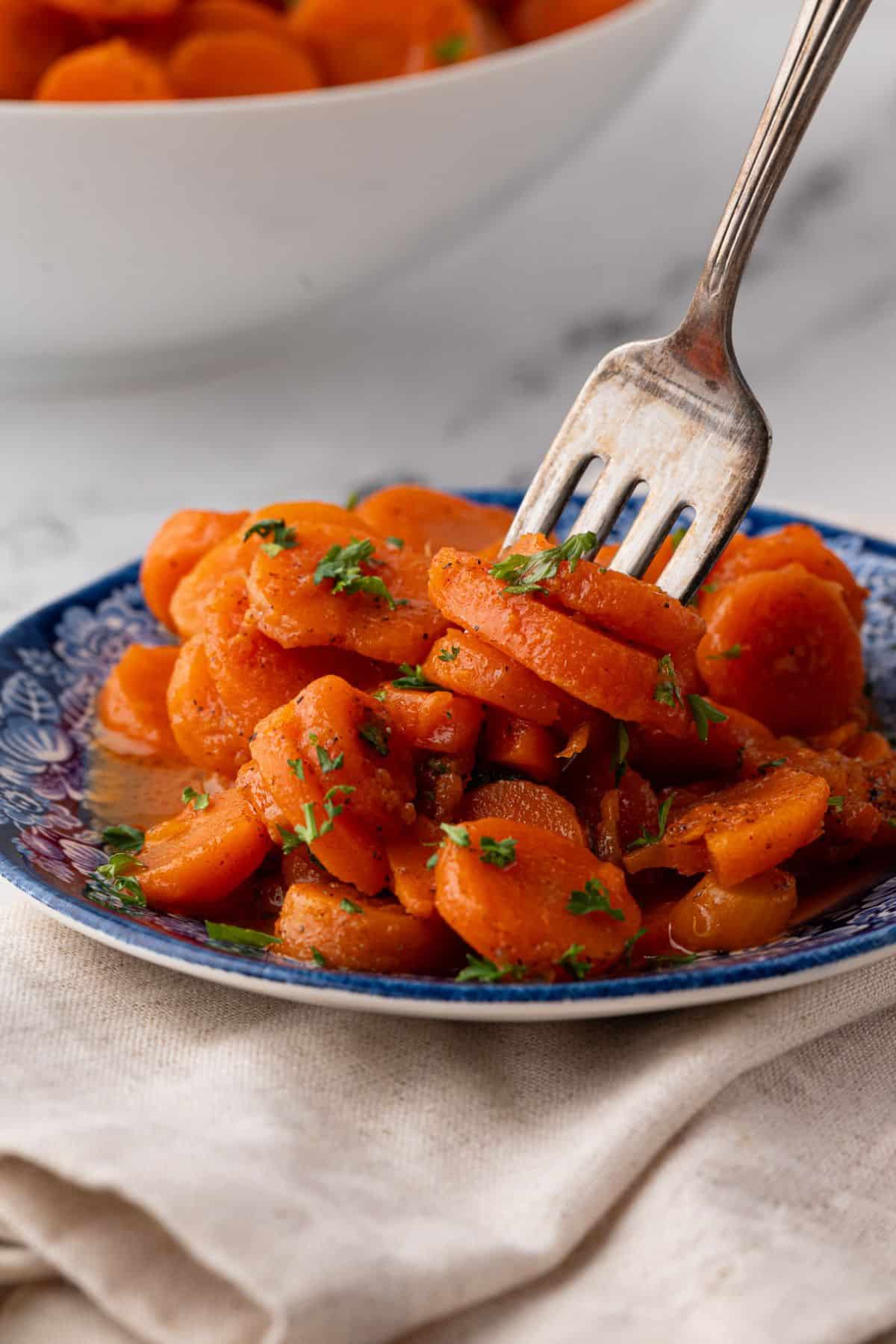 A close-up of a forkful of tender, seasoned carrot slices from a serving plate.