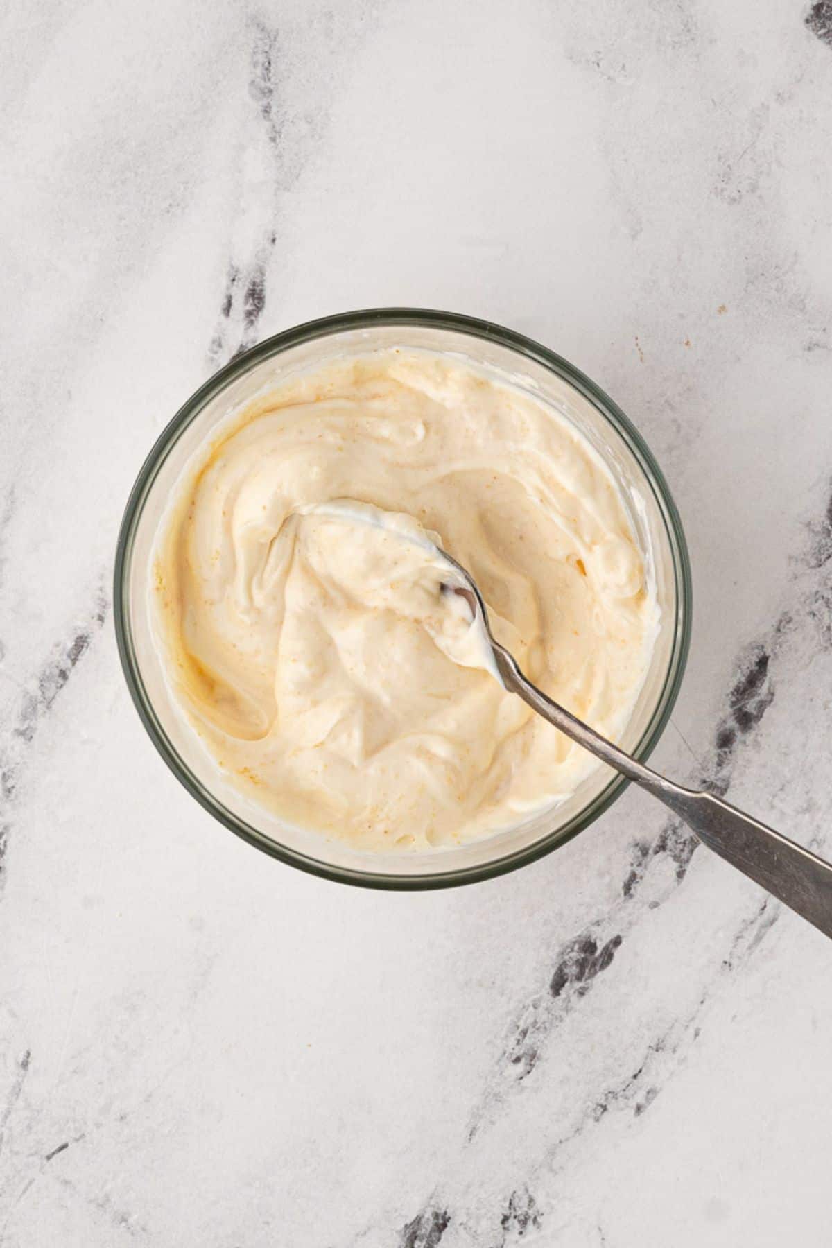 Creamy mayonnaise-based mixture in a glass bowl with a spoon for spreading.