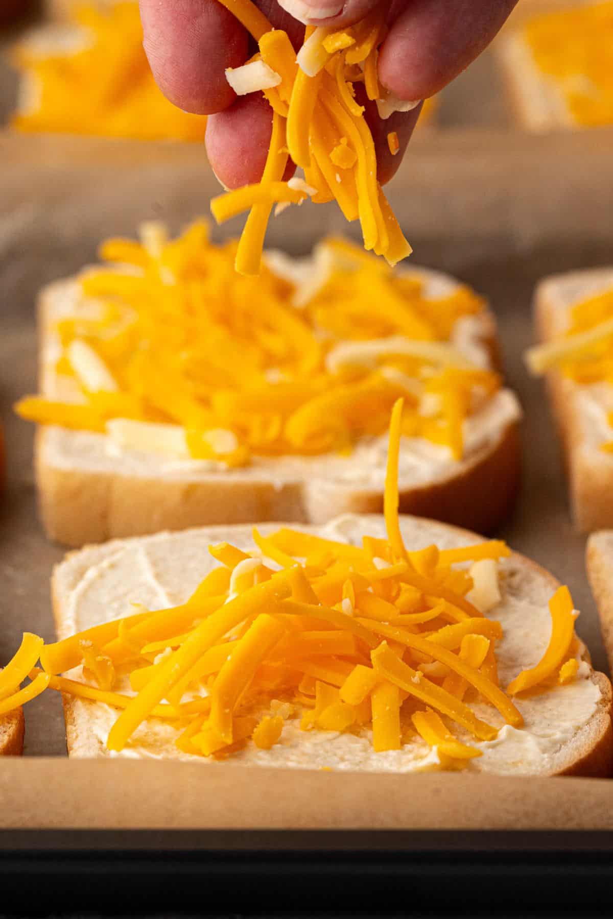 A hand sprinkling shredded cheddar cheese onto slices of bread.