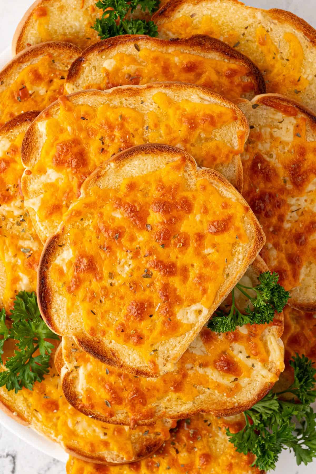Pile of golden, cheesy toasts garnished with fresh parsley on a plate.