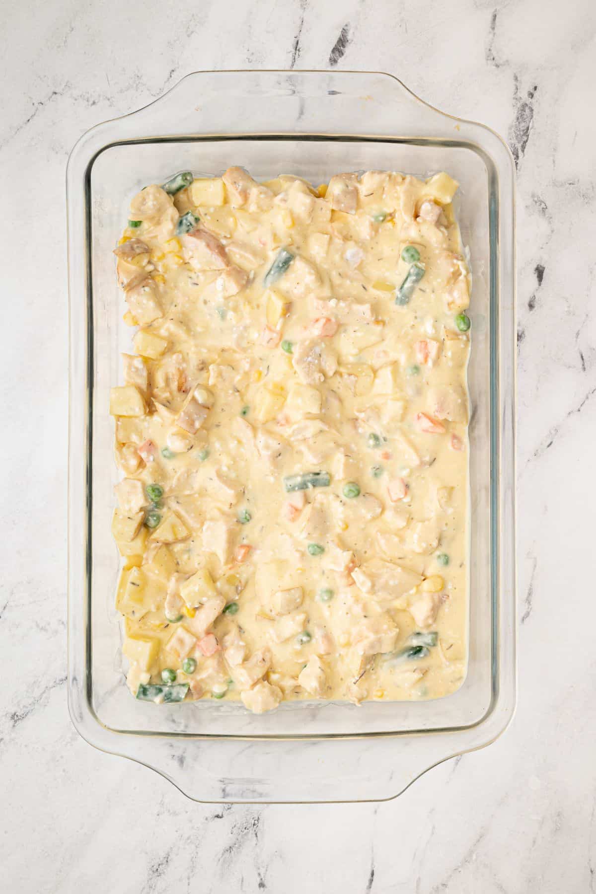 The creamy chicken and vegetable mixture spread evenly in a glass baking dish before adding the biscuit topping.