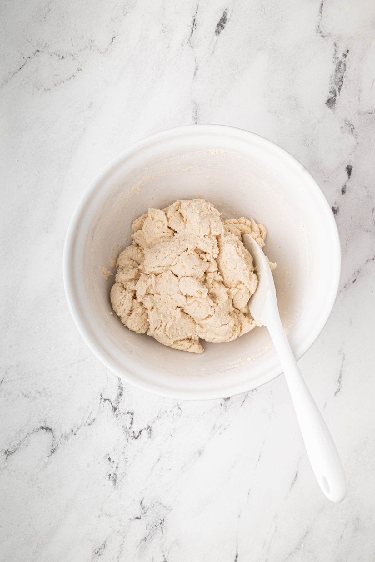 A bowl containing biscuit dough with a white spatula.