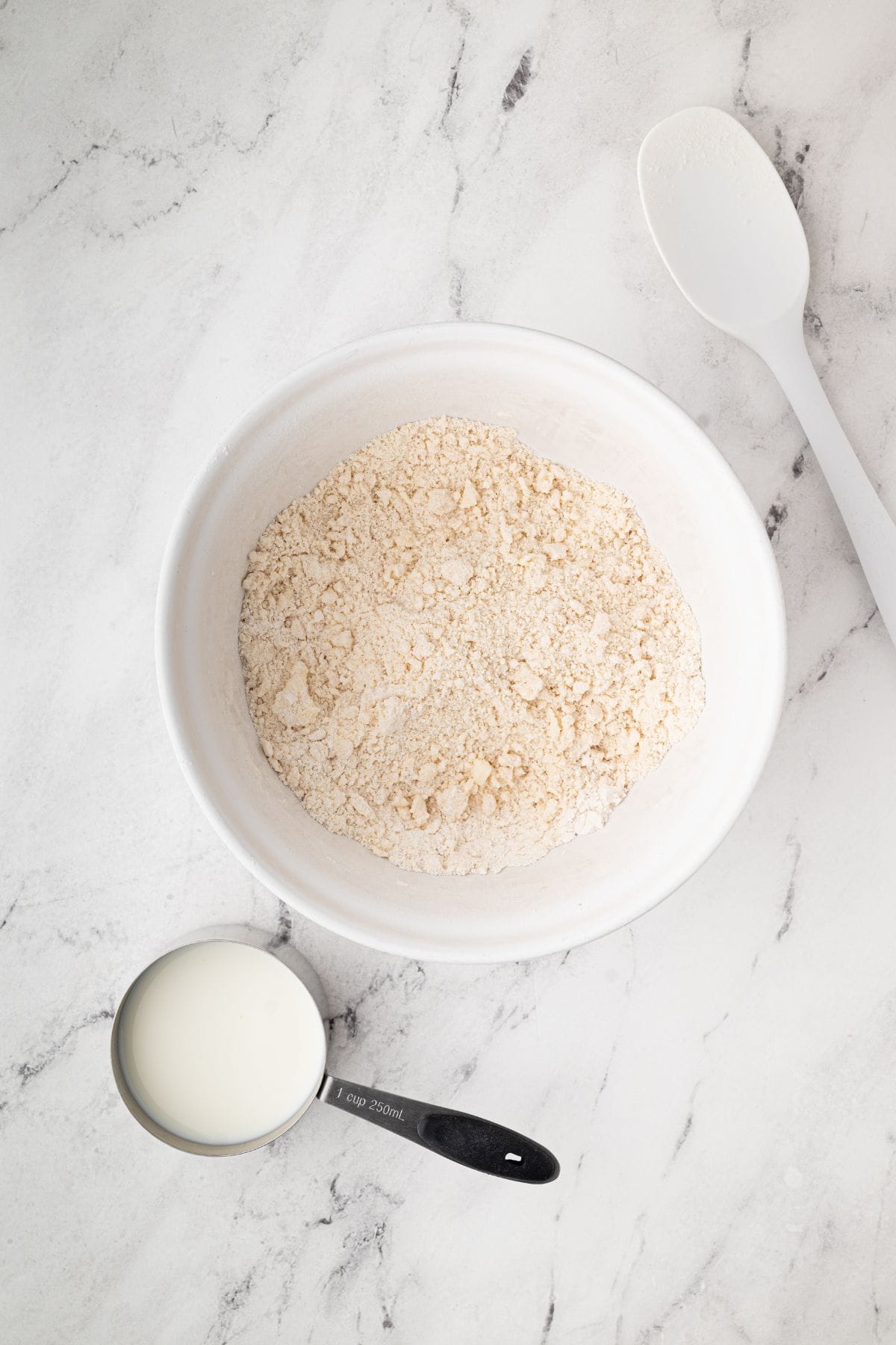 A bowl with dry ingredients (flour mixture) and a measuring cup filled with milk.