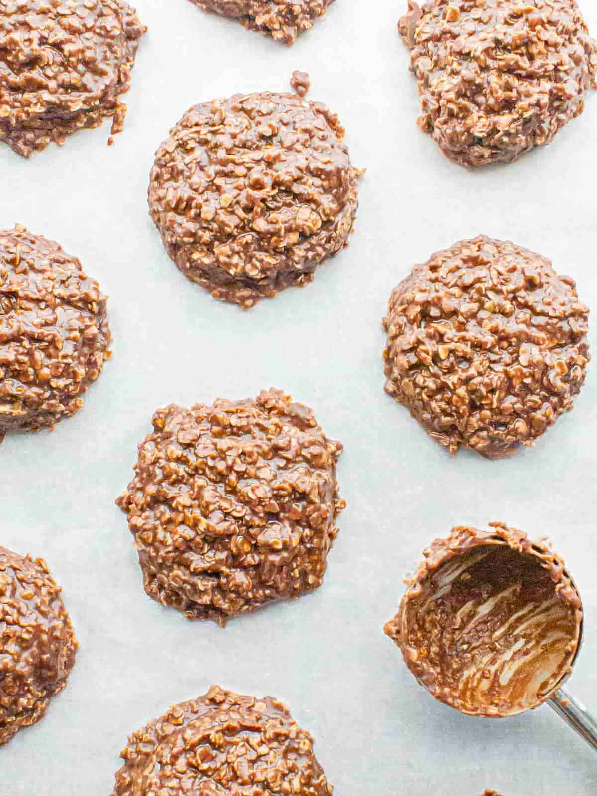 Freshly scooped no-bake chocolate oatmeal cookies set on parchment paper, with a used cookie scoop in the corner.