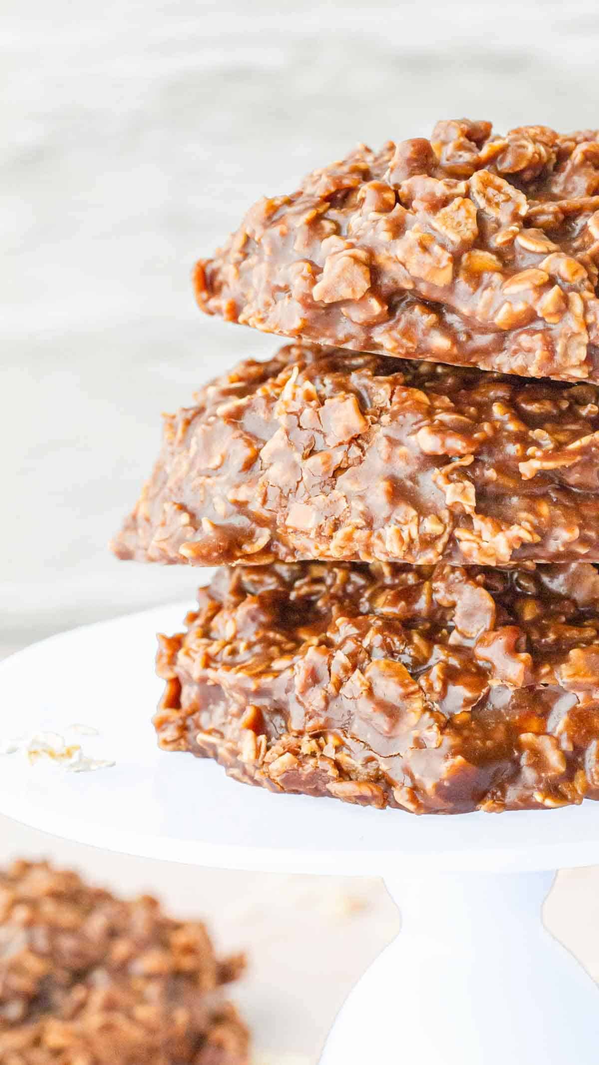 A tall stack of chocolate no-bake cookies on a white cake stand, highlighting their glossy texture.