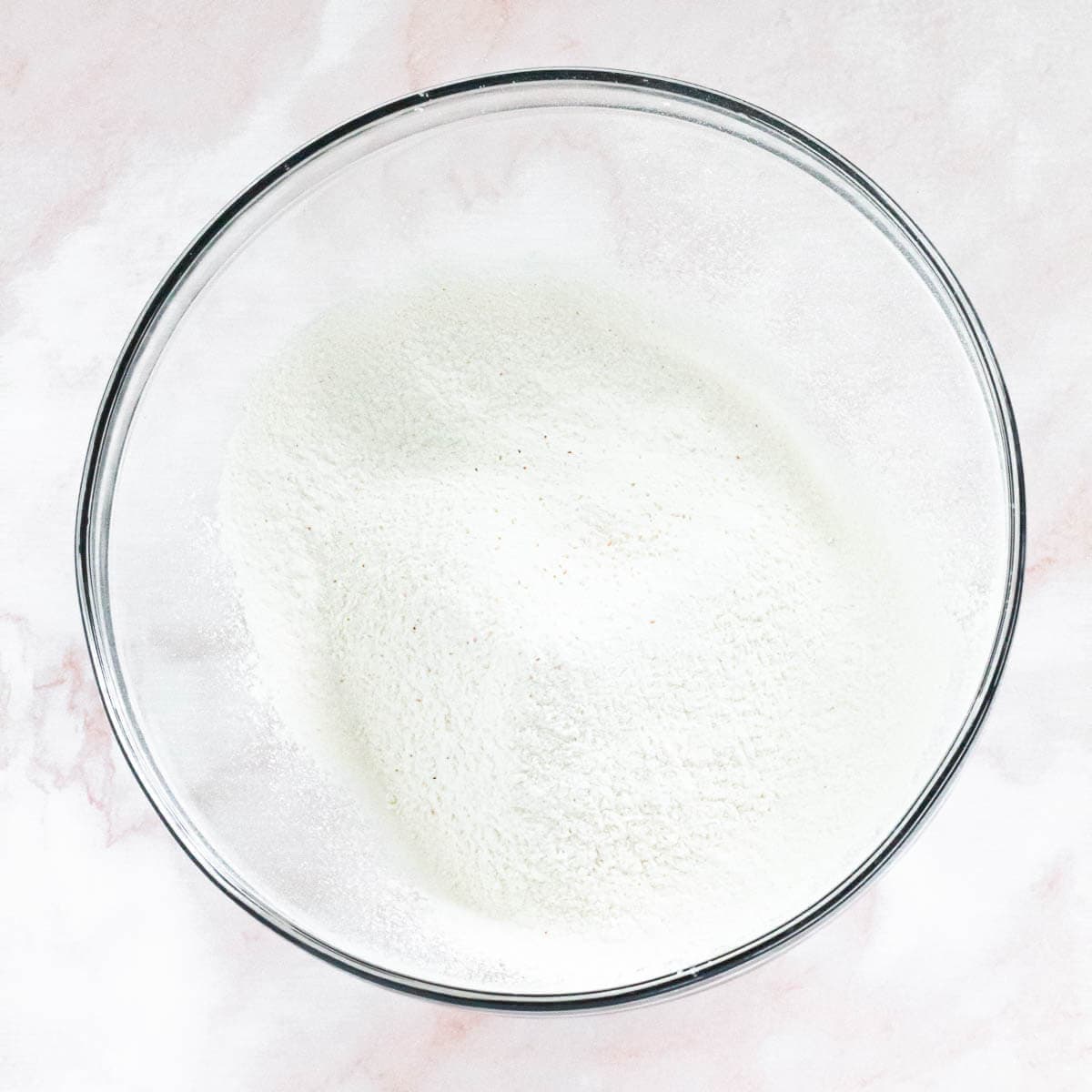 A clear bowl filled with sifted flour, creating a smooth, even texture.