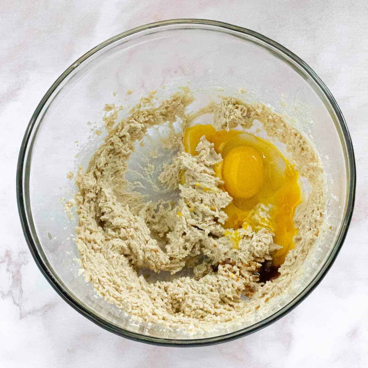 A bowl with creamed butter and sugar, now with eggs and vanilla extract added in.