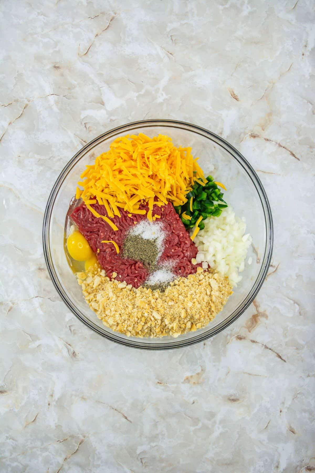 a large bowl containing ground beef, onion, green pepper, eggs, cheese, milk, crushed Ritz crackers, salt, and pepper