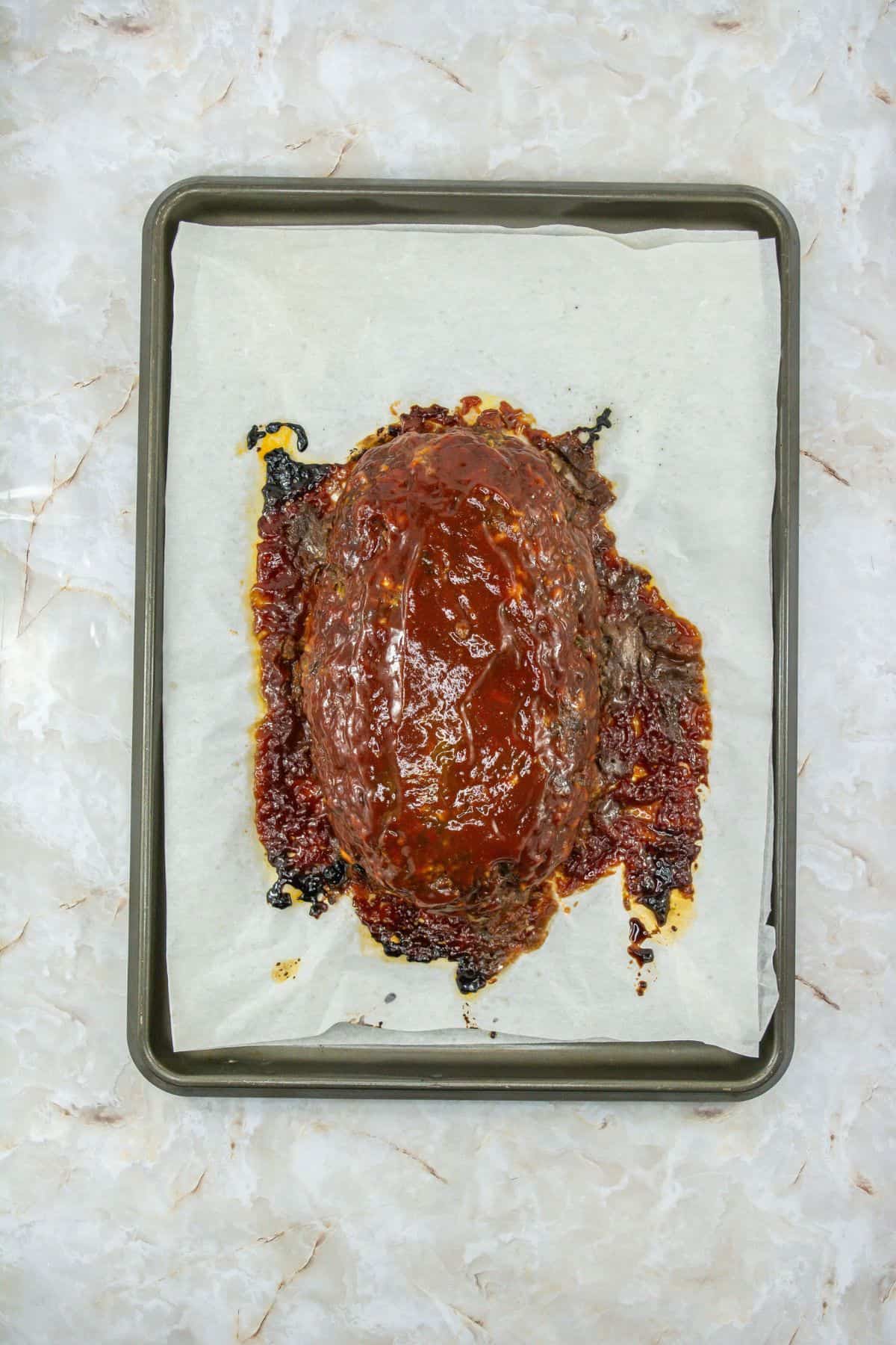 baked meatloaf mixture coated with glaze on a parchment-lined baking sheet