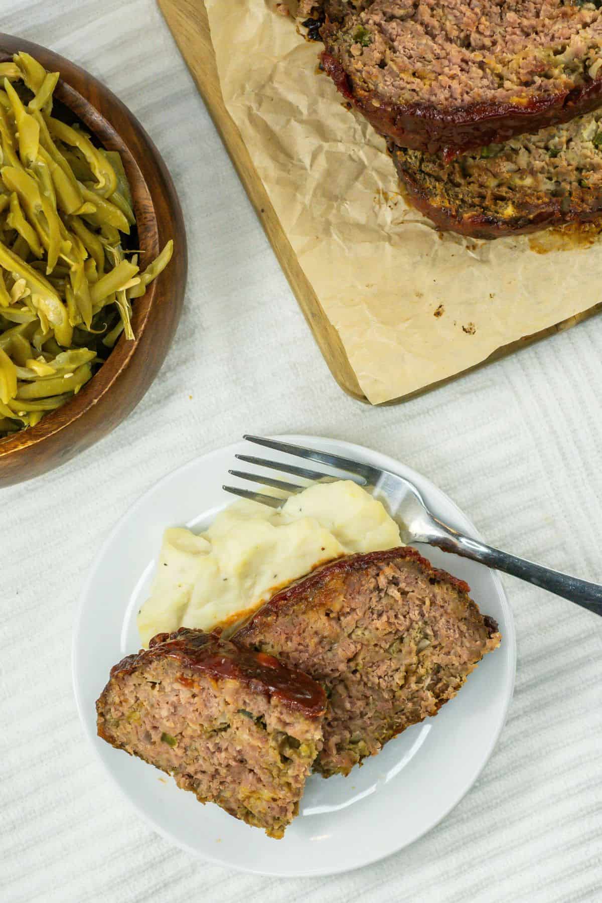 overhead shot of a white plate with two slices of copycat cracker barrel meatloaf and a serving of mashed potatoes, with a fork resting on the plate