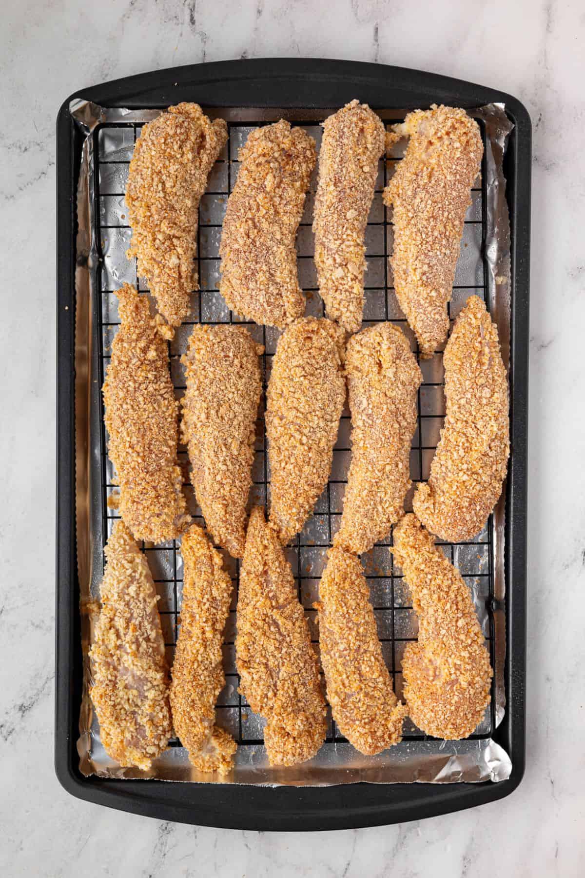 Breaded tenders arranged on a baking tray with a wire rack.