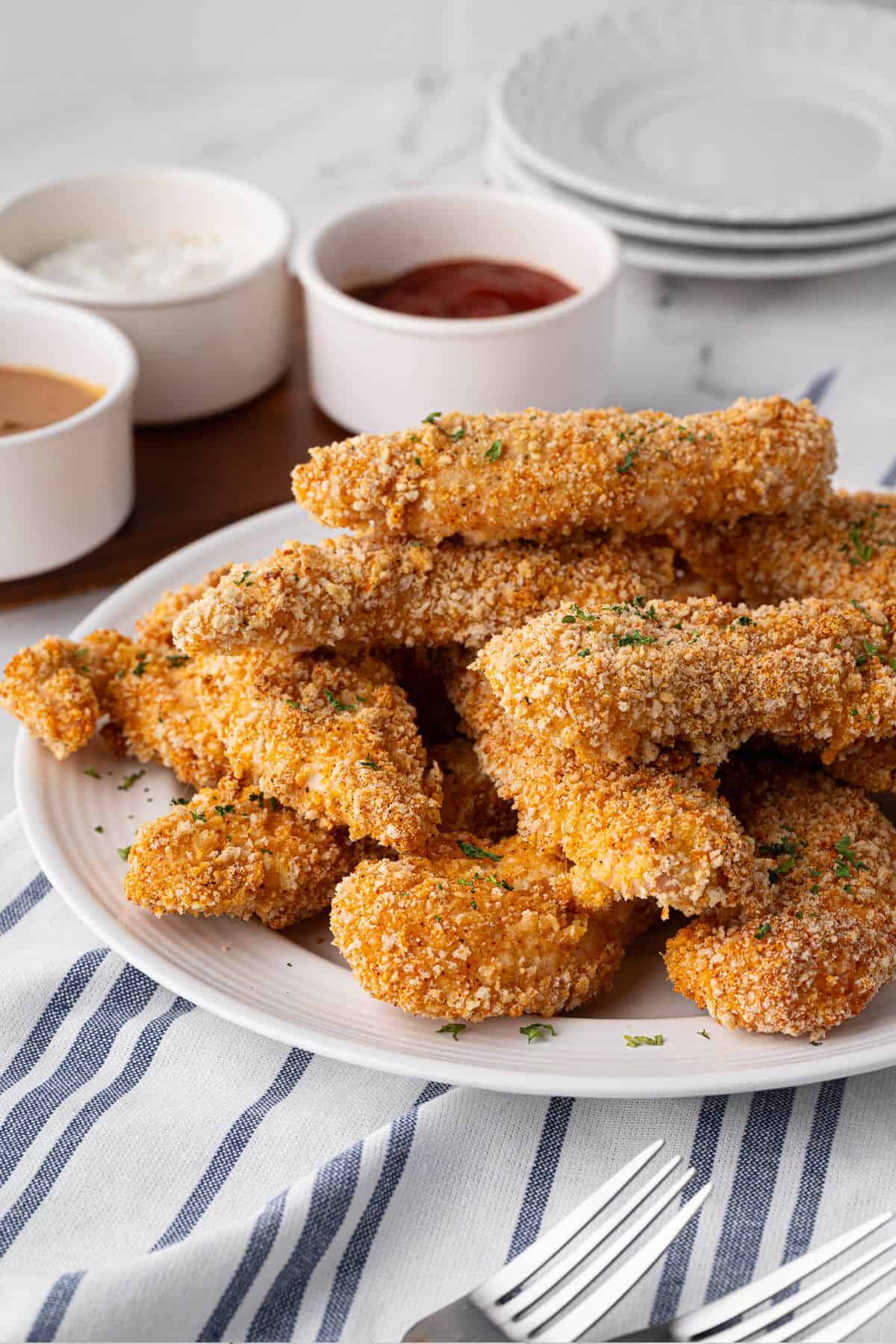 Golden, crispy chicken tenders served on a plate with dipping sauces.