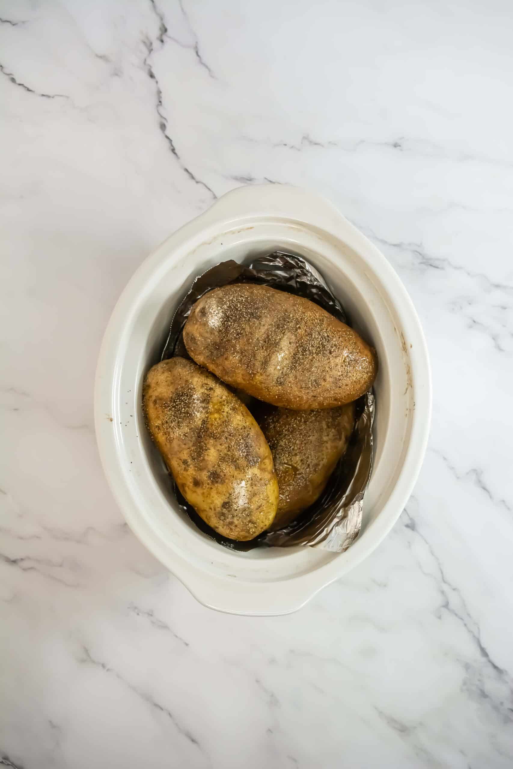 four russet potatoes stacked in a slow cooker on top of each other